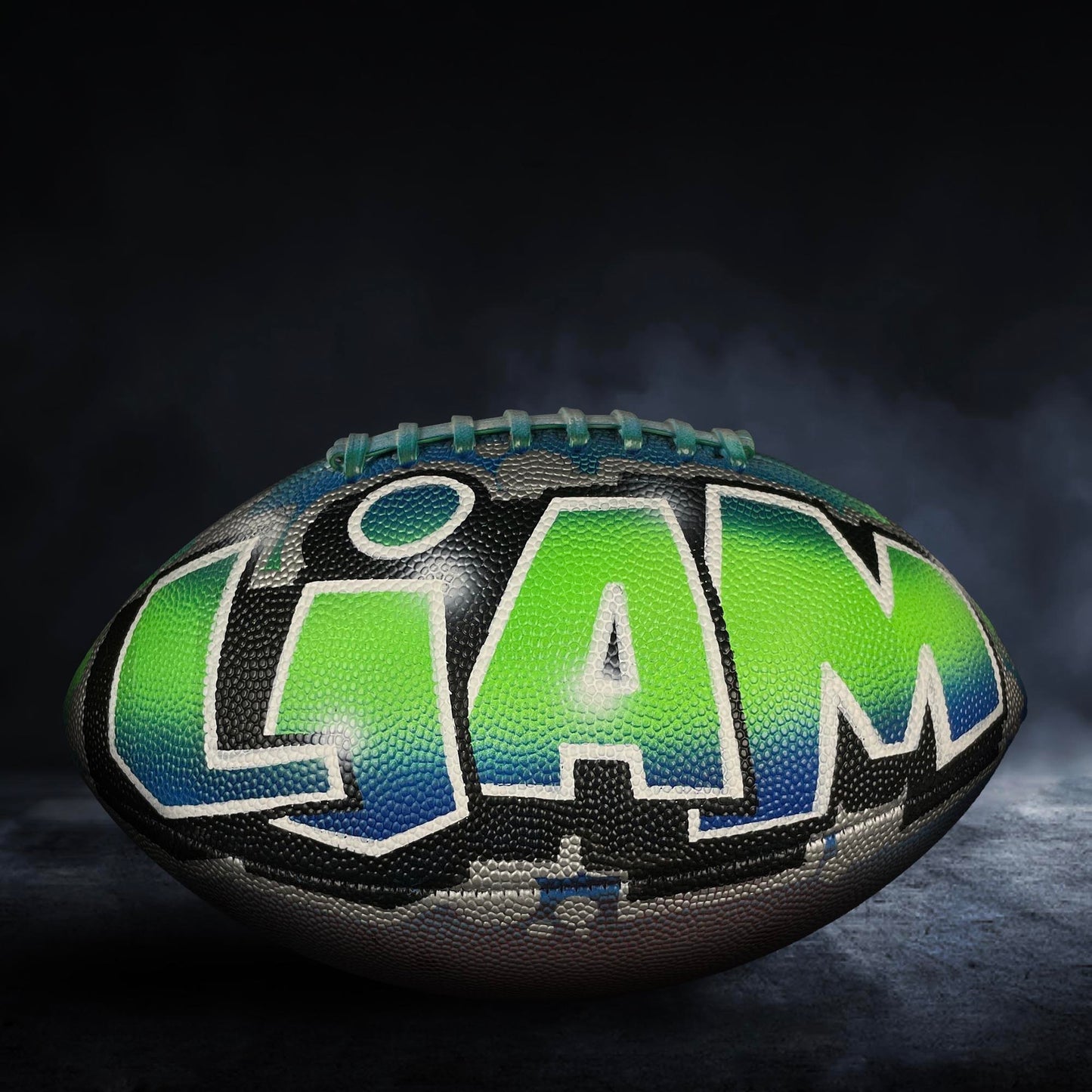 A football with the word "Liam" painted on it, sitting on a dark surface with smoke or fog in the background.