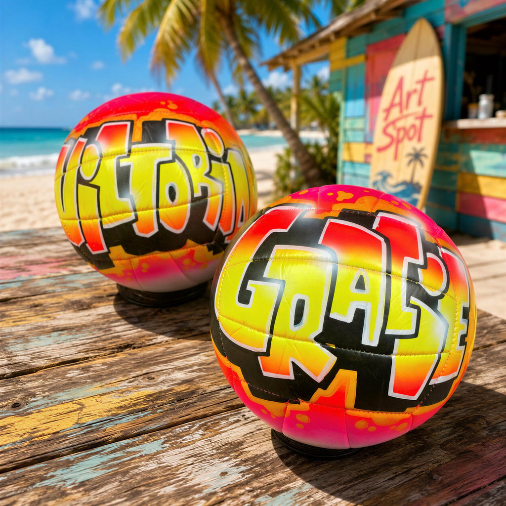 Two colorful beach balls with graffiti-style writing on them, placed on a weathered wooden surface with a tropical beach and palm trees in the background.