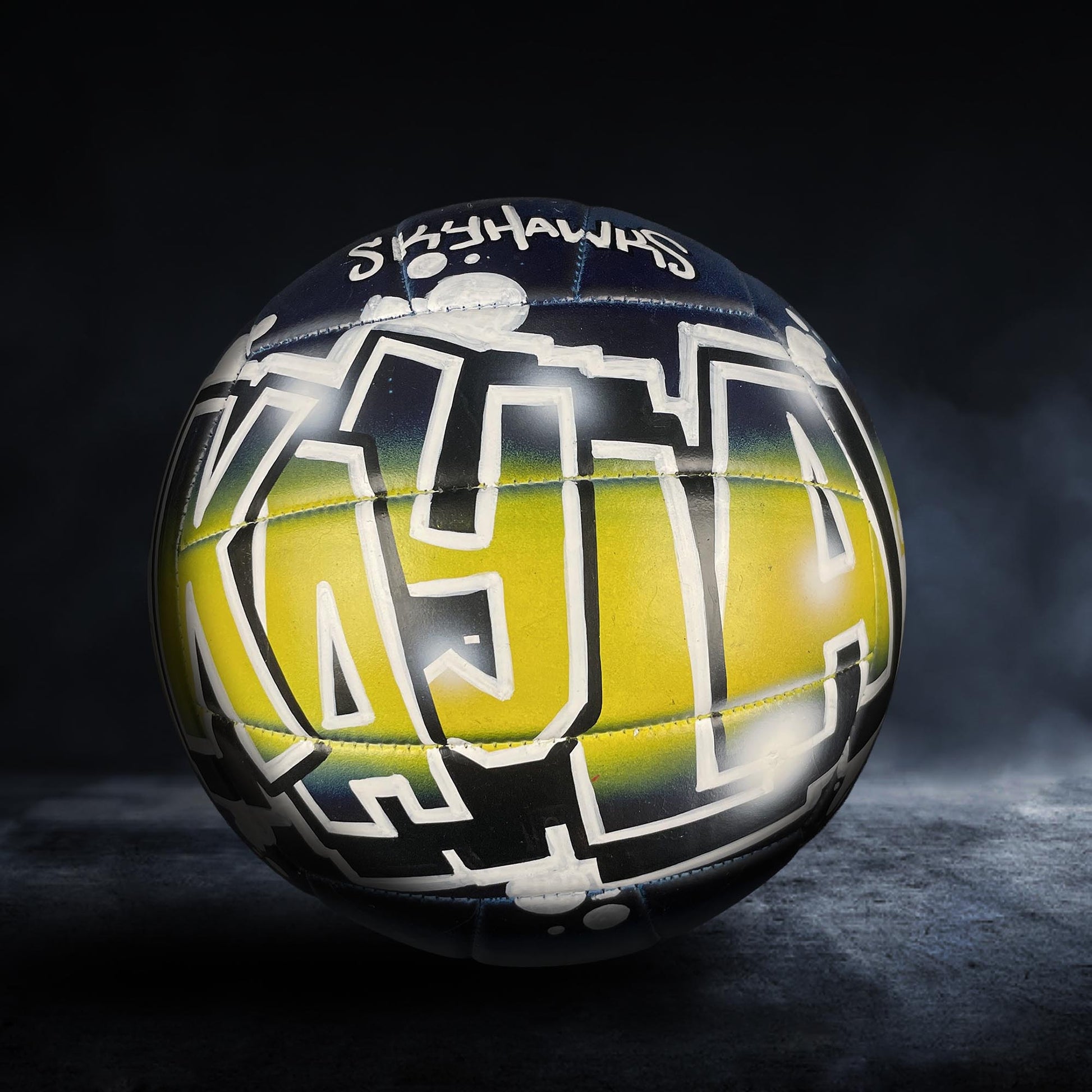 A colorful sports ball with graffiti-style text on it, set against a dark background.