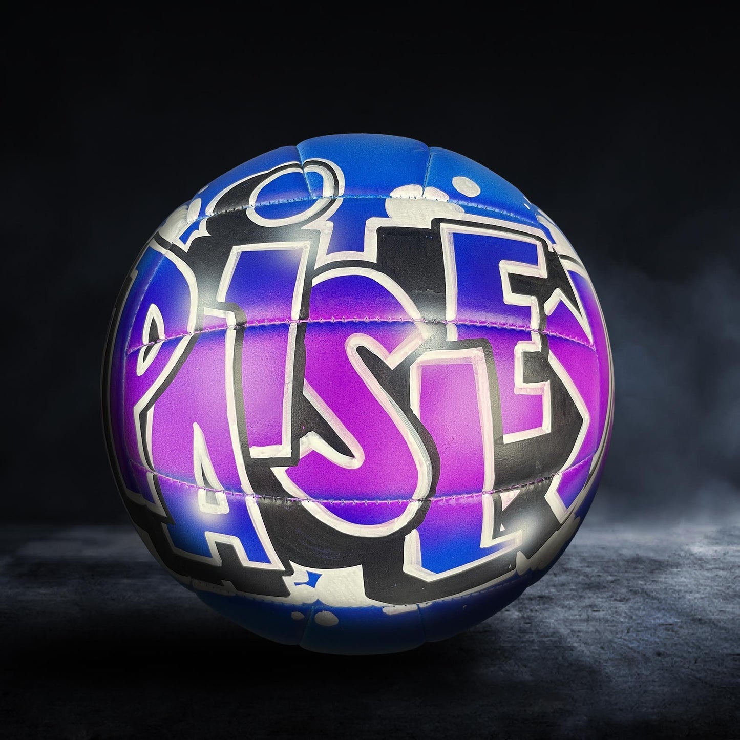 A colorful sports ball with graffiti-style text on it, set against a dark background.