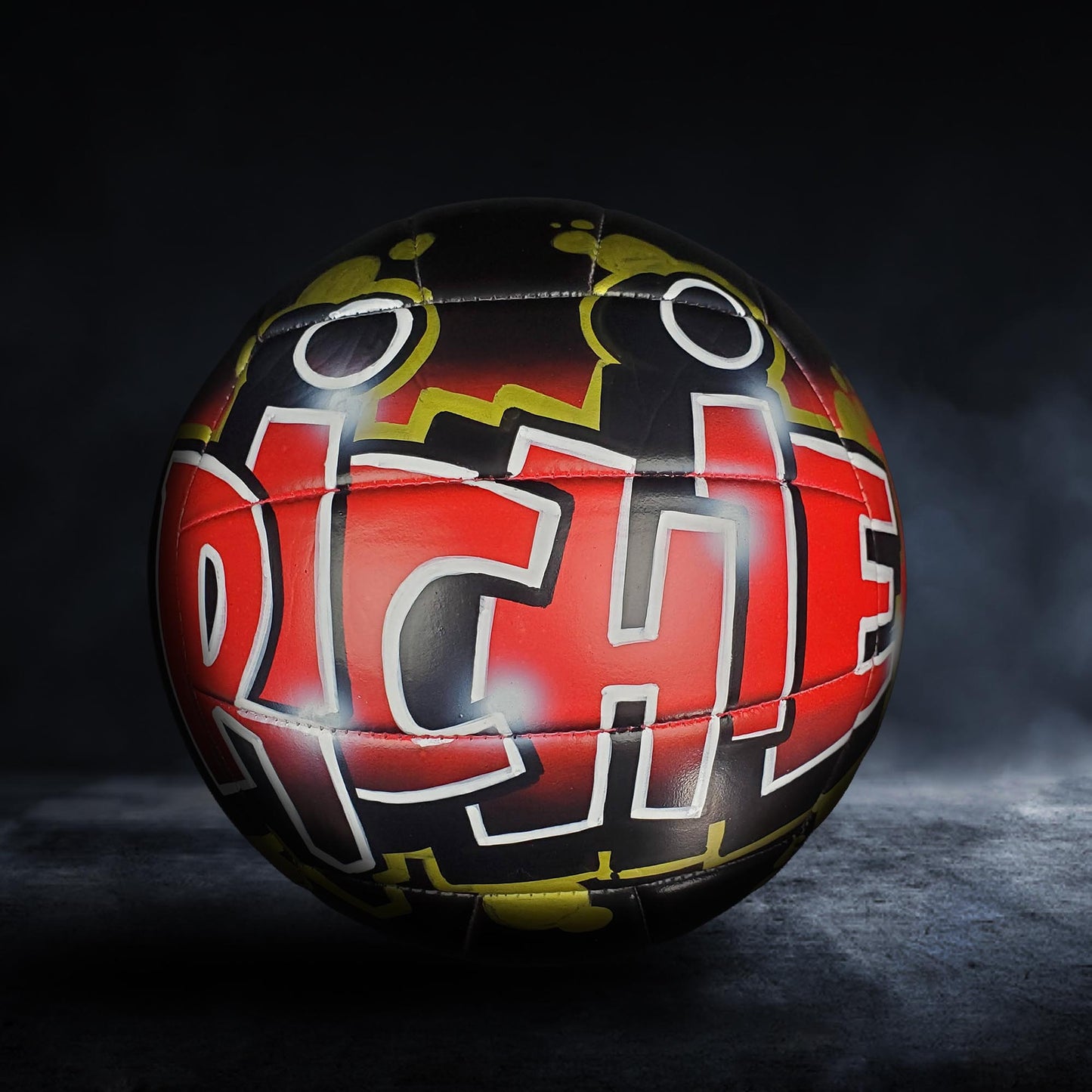 A colorful soccer ball with graffiti-style text on it, set against a dark background.