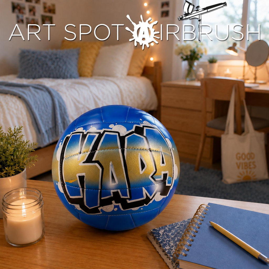 a bedroom with a bed, a desk, and various personal items such as a candle, a notebook, and a personalized custom volleyball with graffiti on it.