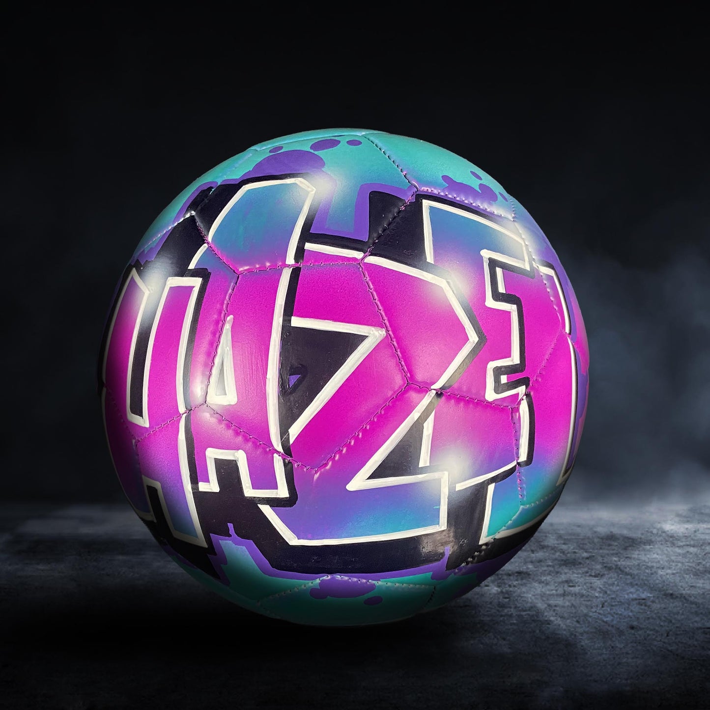 A colorful soccer ball with a graffiti-style design on it, featuring the letters "AZZ" in pink and blue.