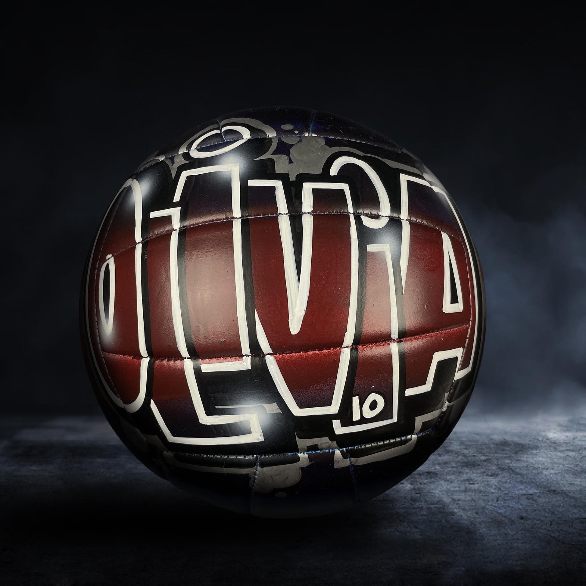 A soccer ball with the word "OLIVIA" painted on it, against a dark background.