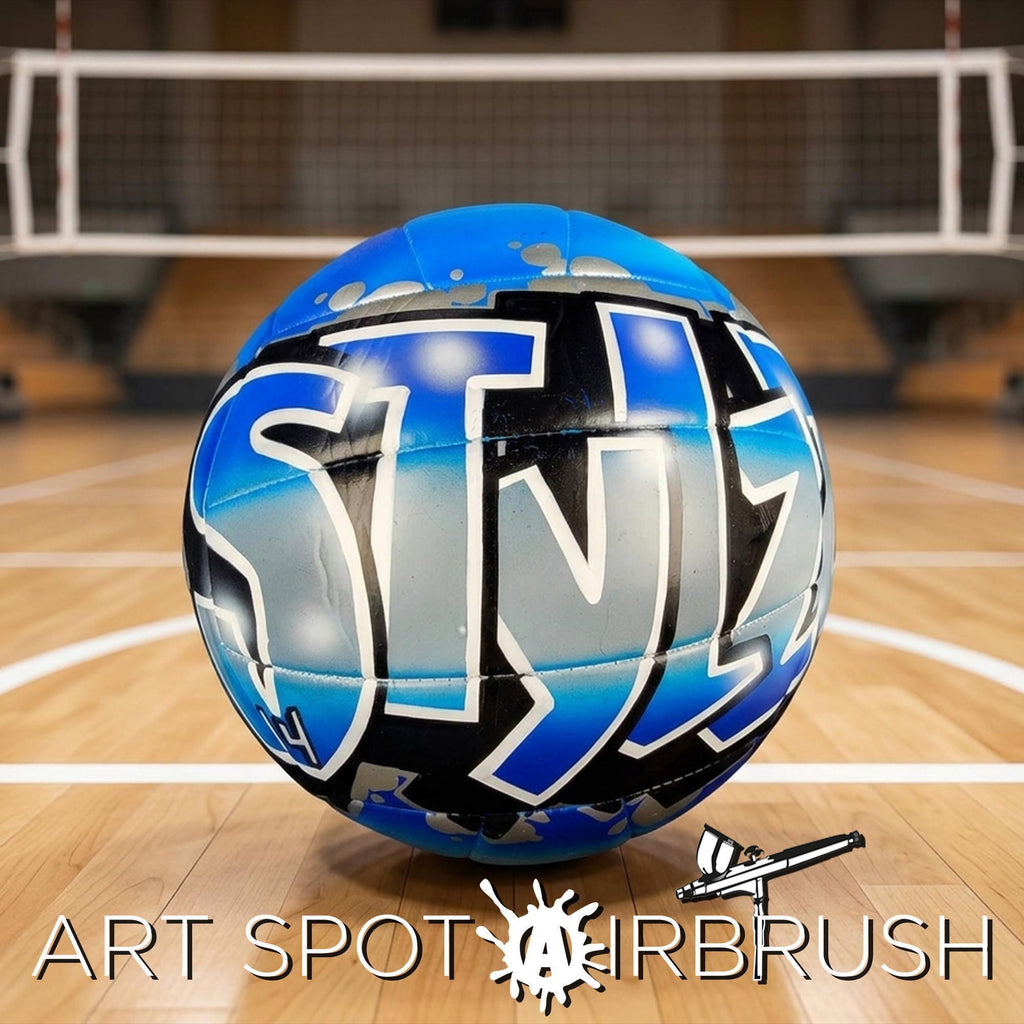 A blue and black custom volleyball with the word "STYLZZ" painted on it, sitting on a wooden court.