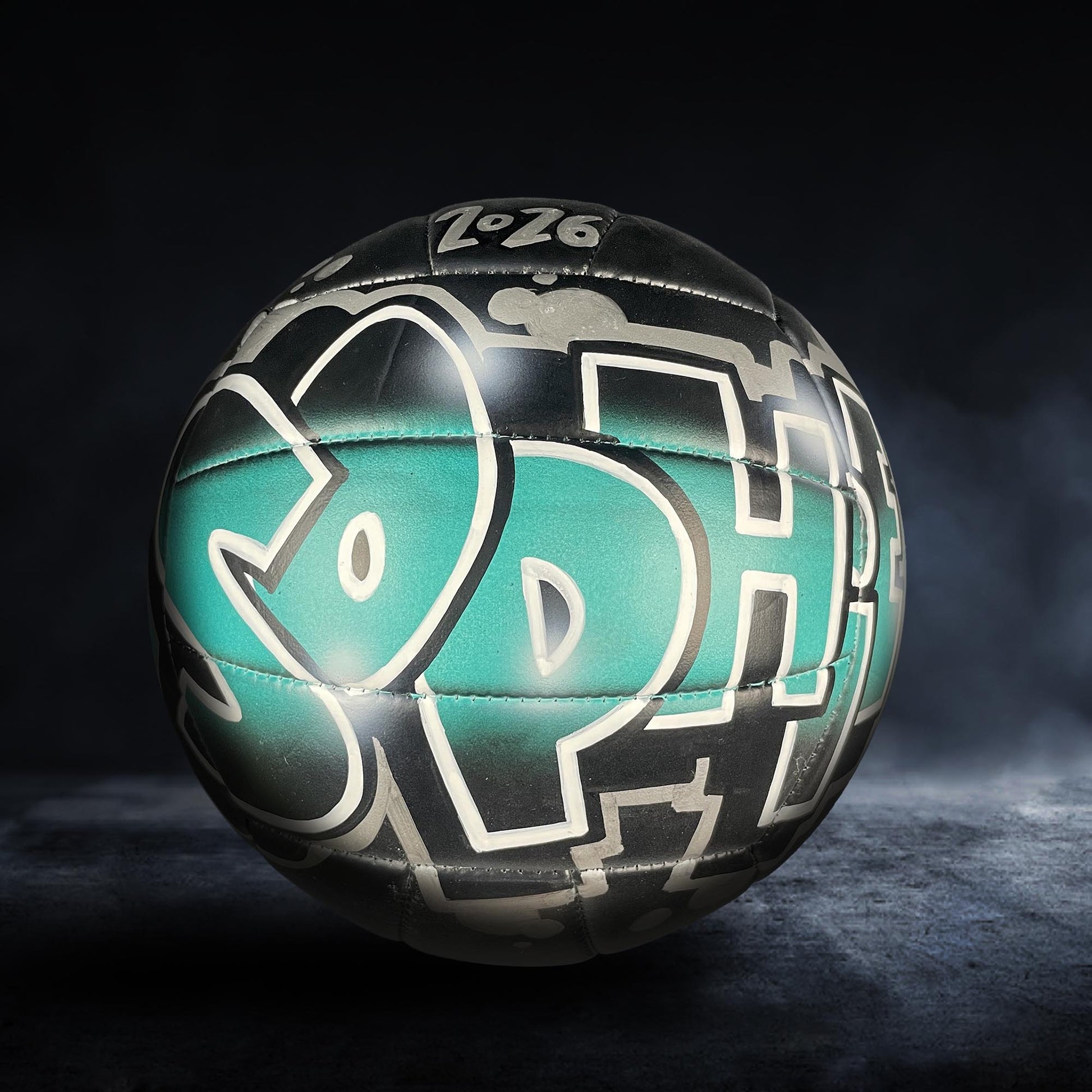 A soccer ball with graffiti-style lettering on it, set against a dark background.