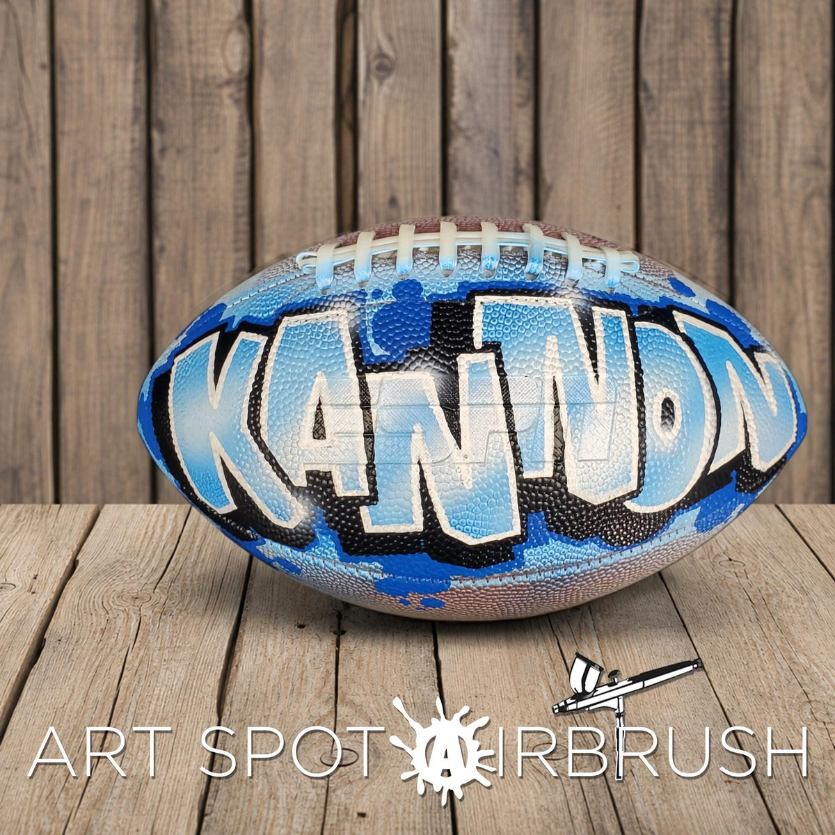 A football with the word "KANNON" painted on it, sitting on a wooden surface.