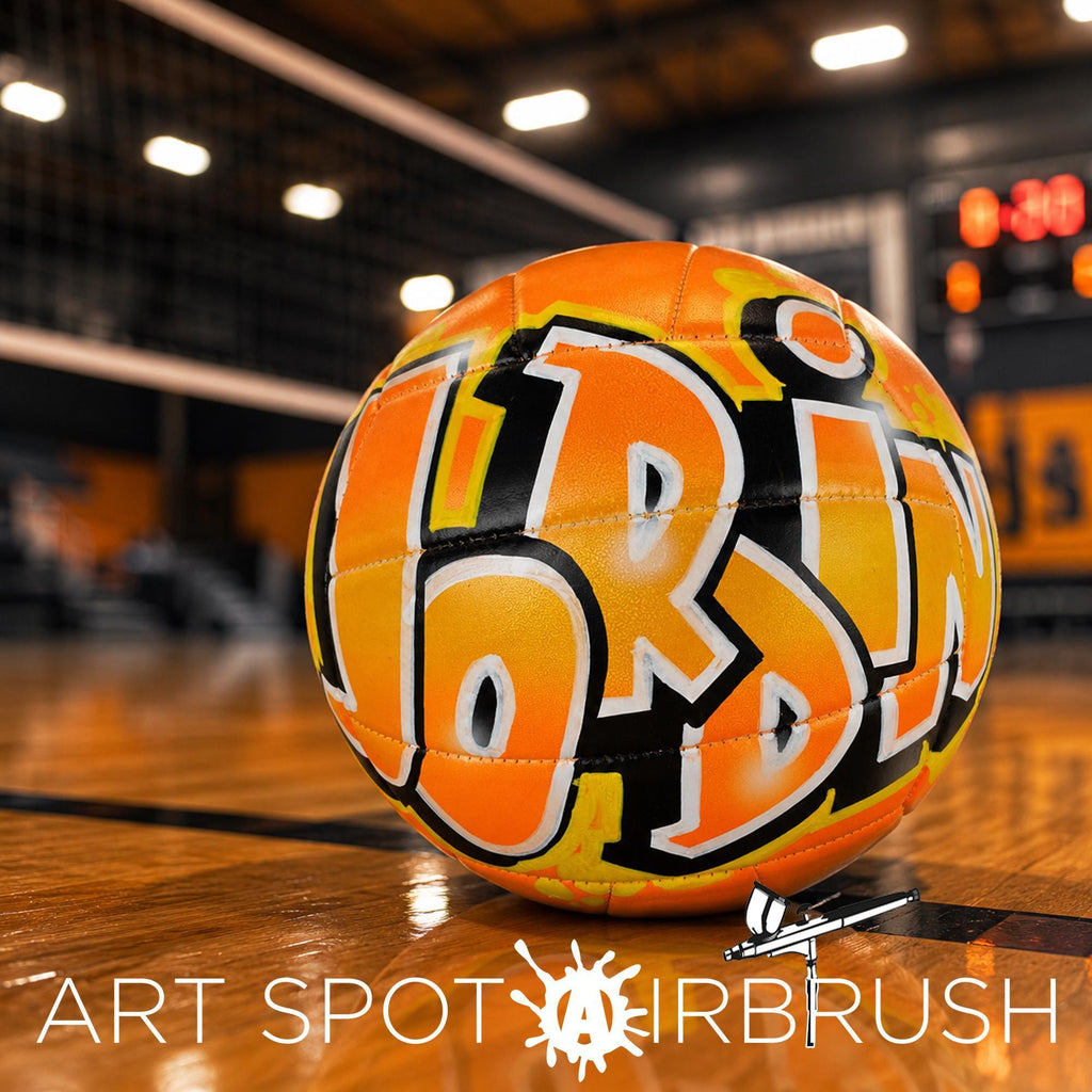 An orange and black custom volleyball personalized with the word "JORDIN" painted on it, sitting on a wooden court.