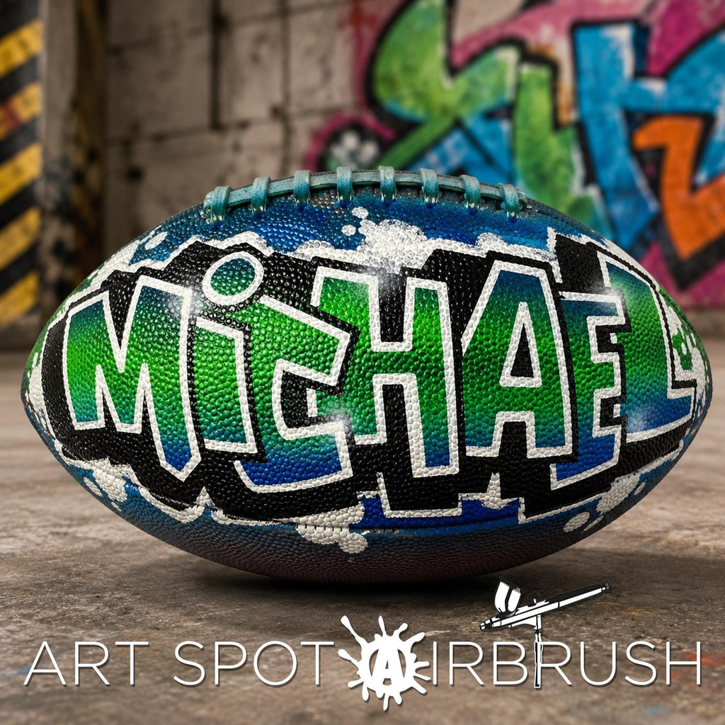 A custom football personalized with the name "Michael" painted on it, sitting on a surface with graffiti in the background.