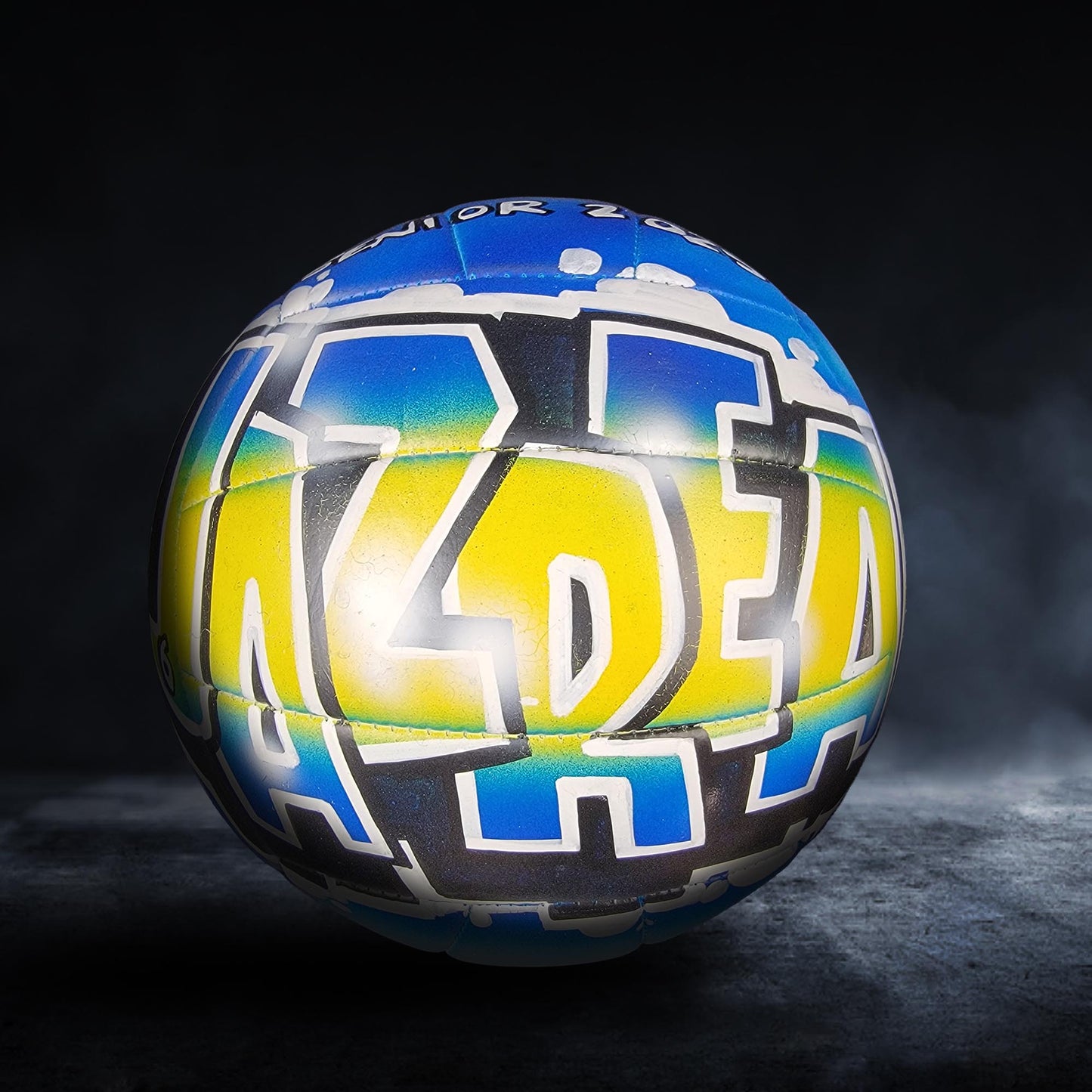 A colorful sports ball with the word "ALDE" painted on it, set against a dark background.