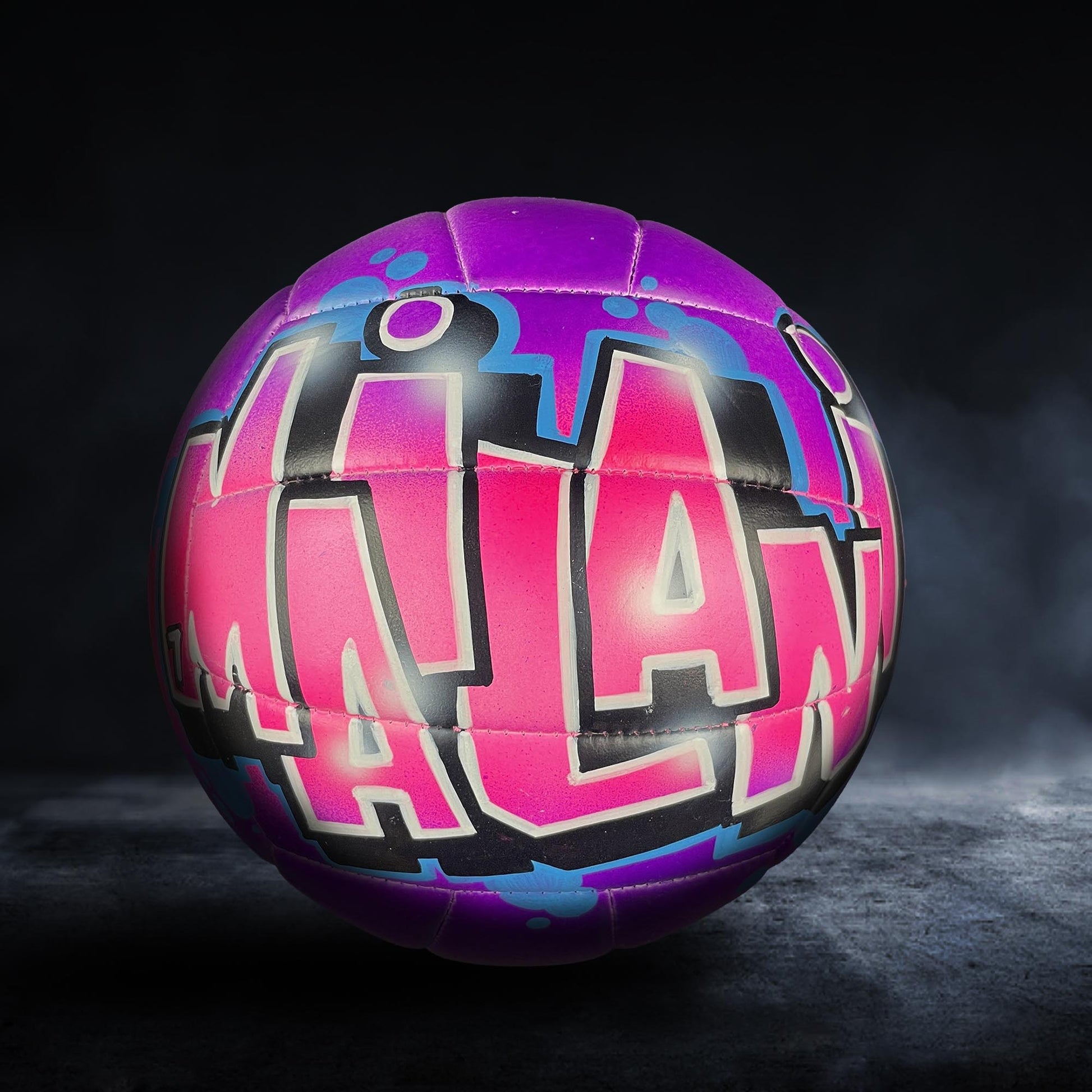 A colorful sports ball with the word "MILAN" painted on it, set against a dark background.