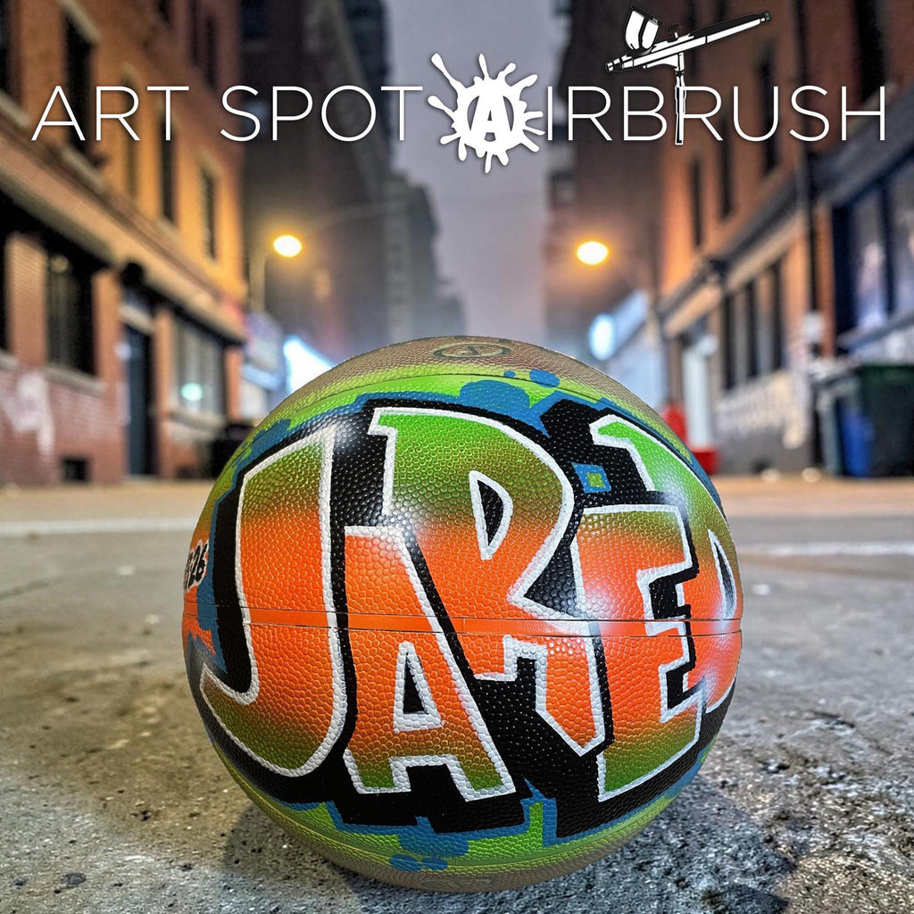 A basketball with the name "Jae" painted on it, sitting on a concrete surface in an urban setting at night.