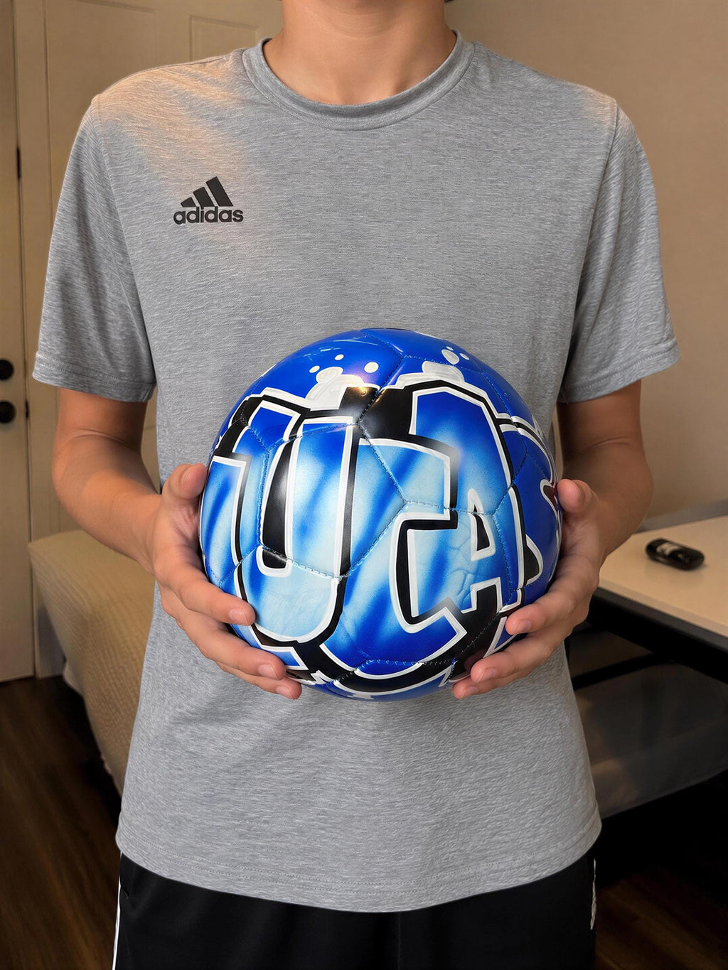A person is holding a blue and black soccer ball with the word "USA" painted on it.