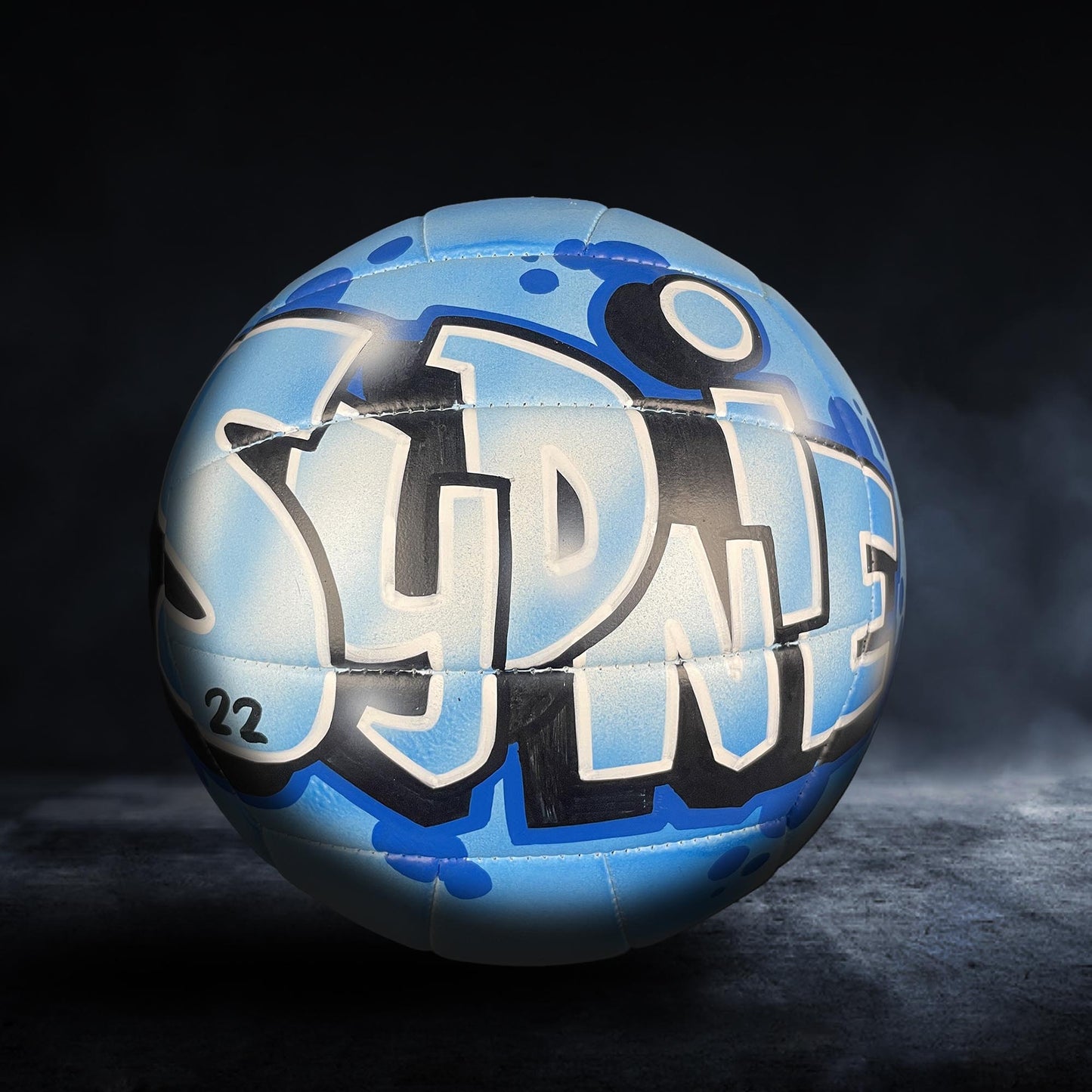 A blue and white sports ball with graffiti text on it, placed on a dark surface.