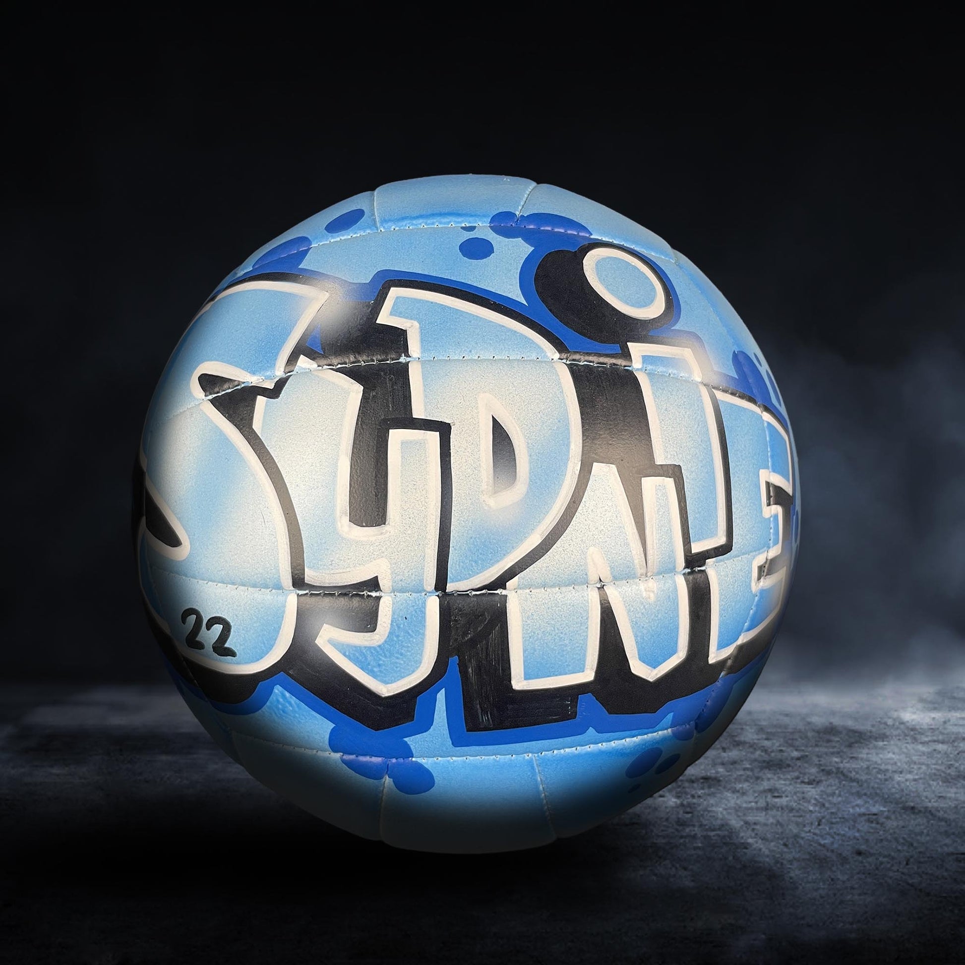 A blue and white sports ball with graffiti text on it, placed on a dark surface.
