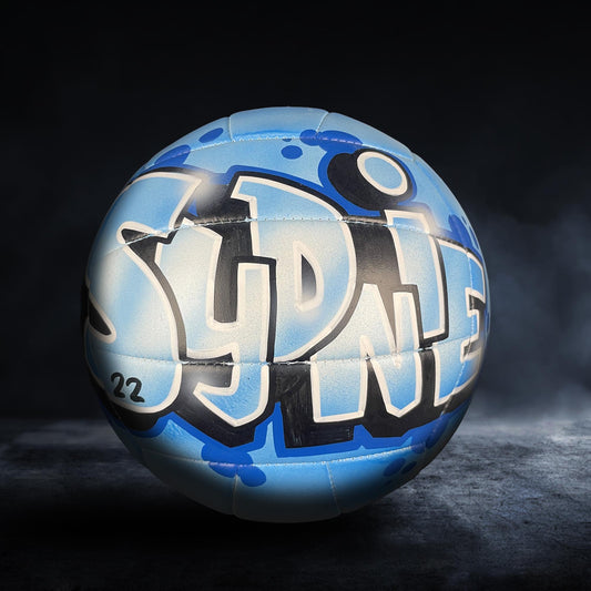 A blue and white sports ball with graffiti text on it, placed on a dark surface.