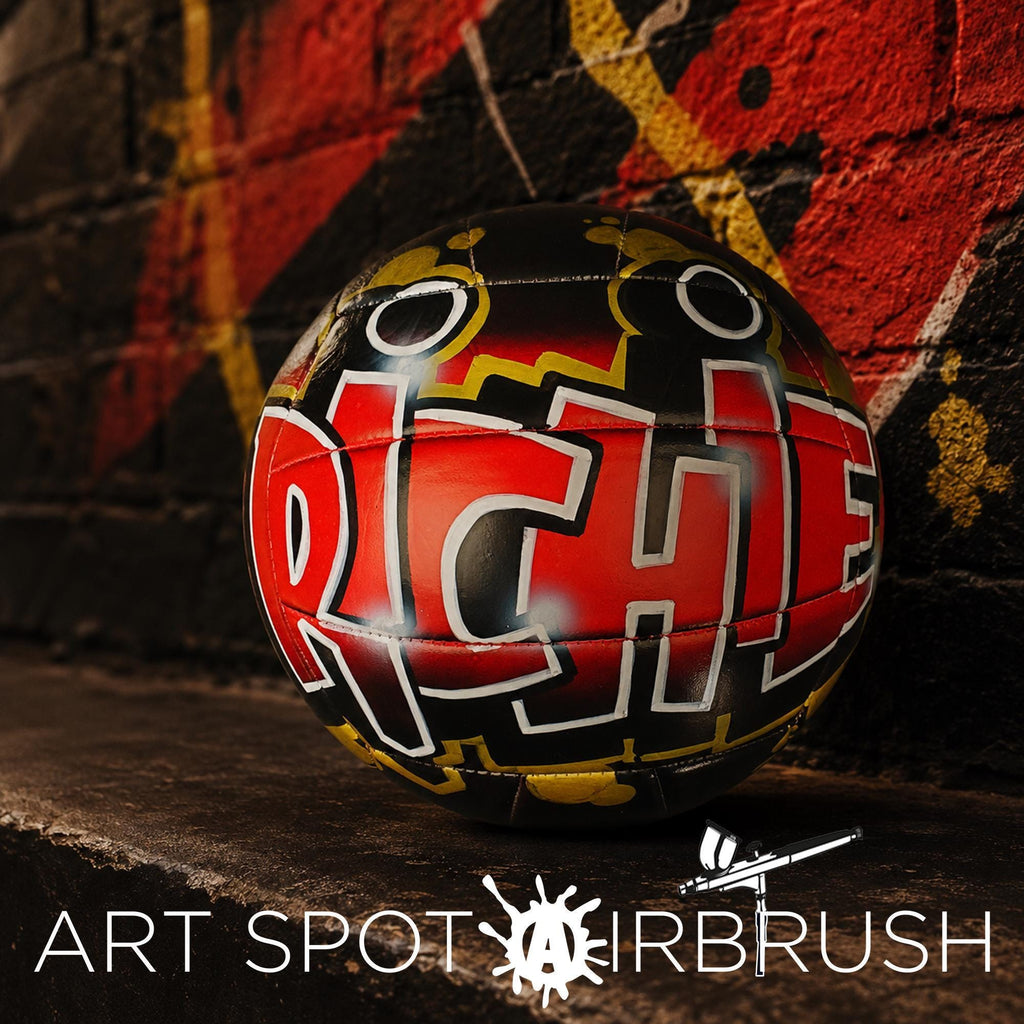 A custom volleyball personalized with graffiti on it, placed against a brick wall with a red and yellow pattern.