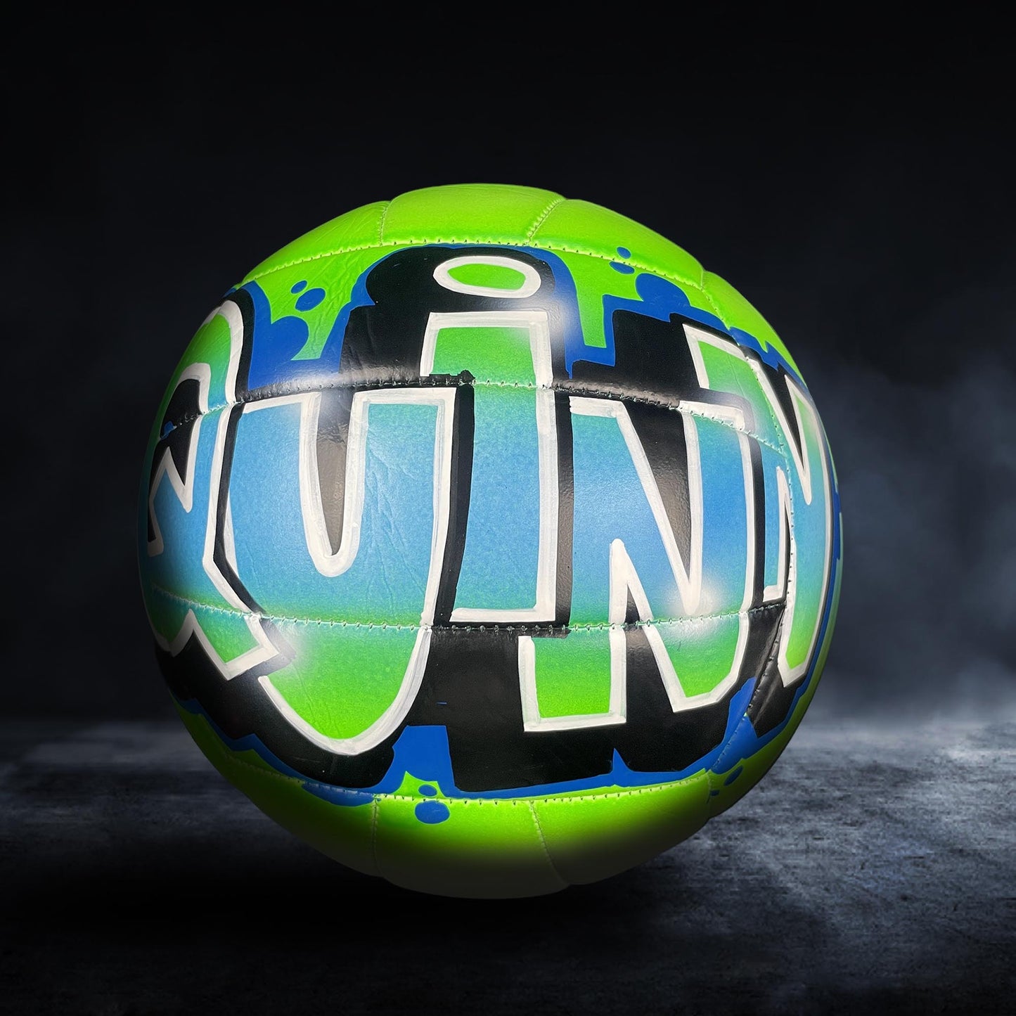A colorful sports ball with the word "QUINN" painted on it, set against a dark background.