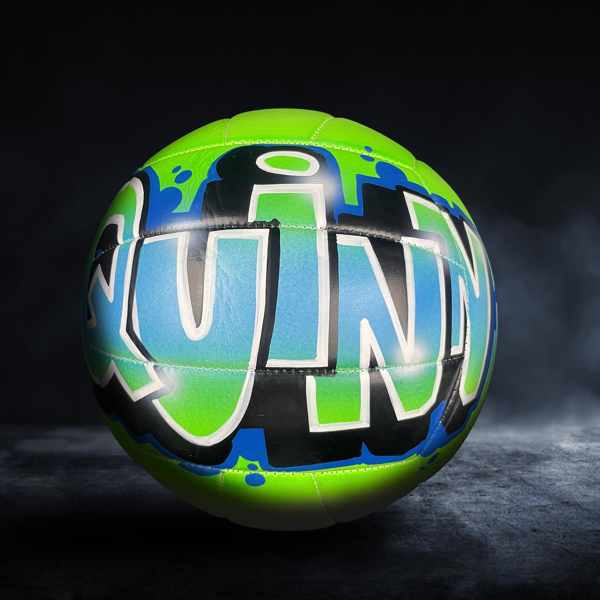 A colorful sports ball with the word "QUINN" painted on it, set against a dark background.