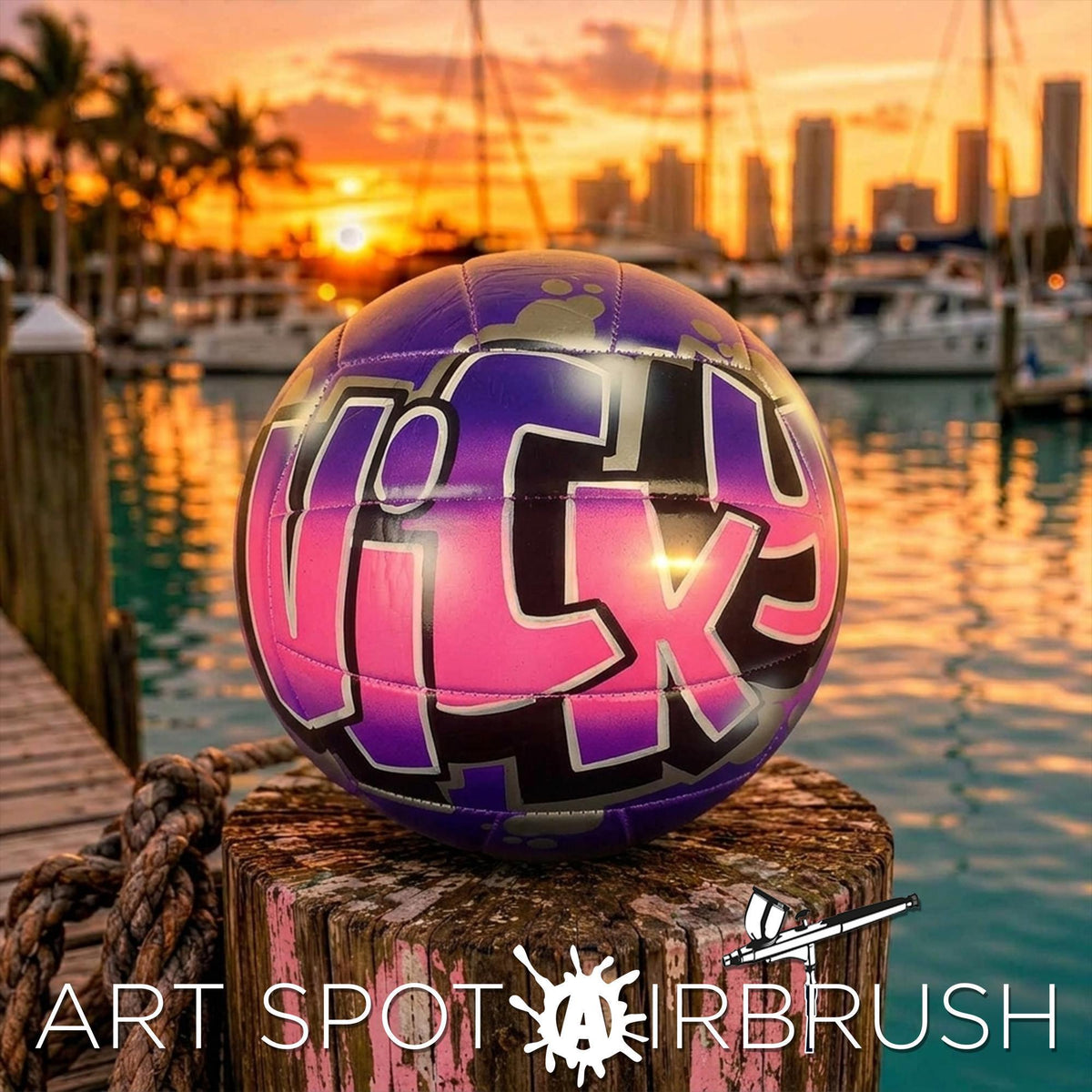 A colorful, graffiti-style personalized custom volleyball is displayed on a wooden post, with a city skyline and boats in the background during a sunset.