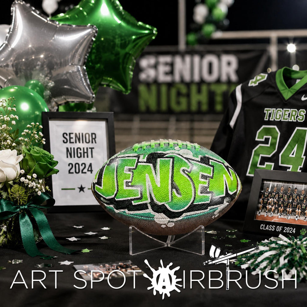 a football with the name " Jensen" painted on it, surrounded by various graduation-related items such as a framed picture, balloons, and a sports jersey.