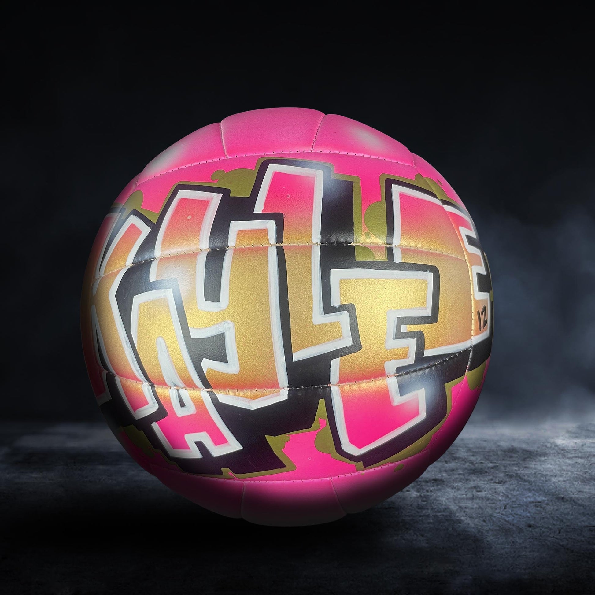 A colorful volleyball with graffiti-style lettering on it, set against a dark background.