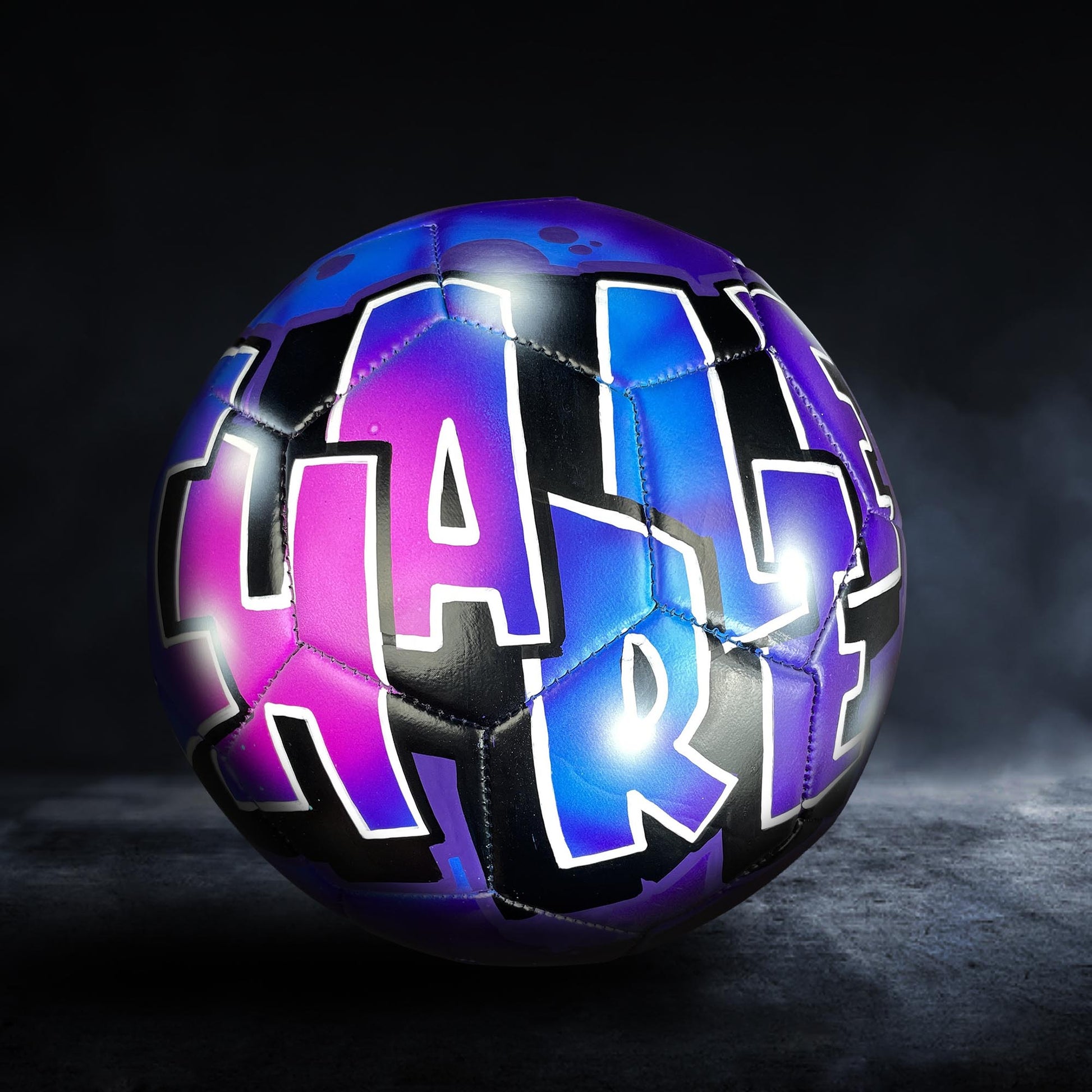 A soccer ball with the word "HARL" painted on it in a colorful, graffiti-style design.