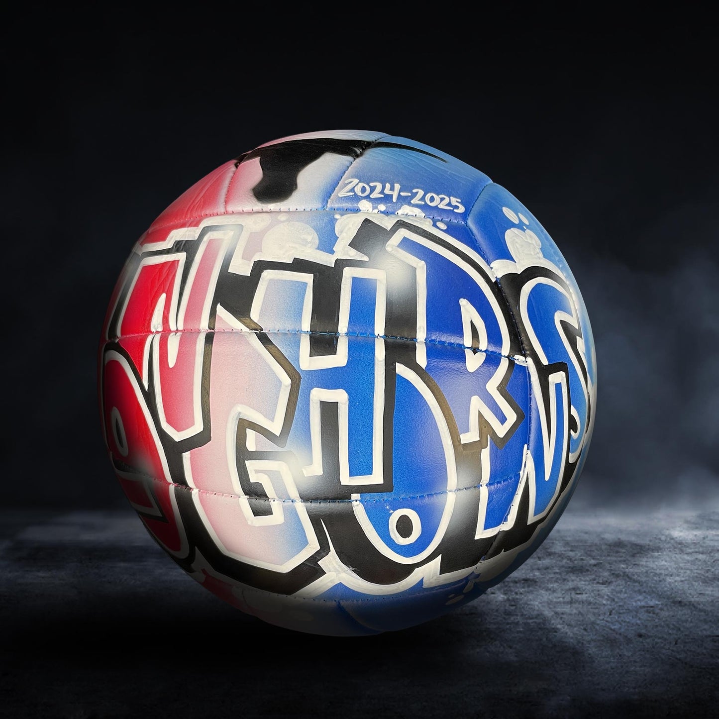 A colorful, graffiti-style soccer ball with the text "2024-2025" painted on it, set against a dark background.