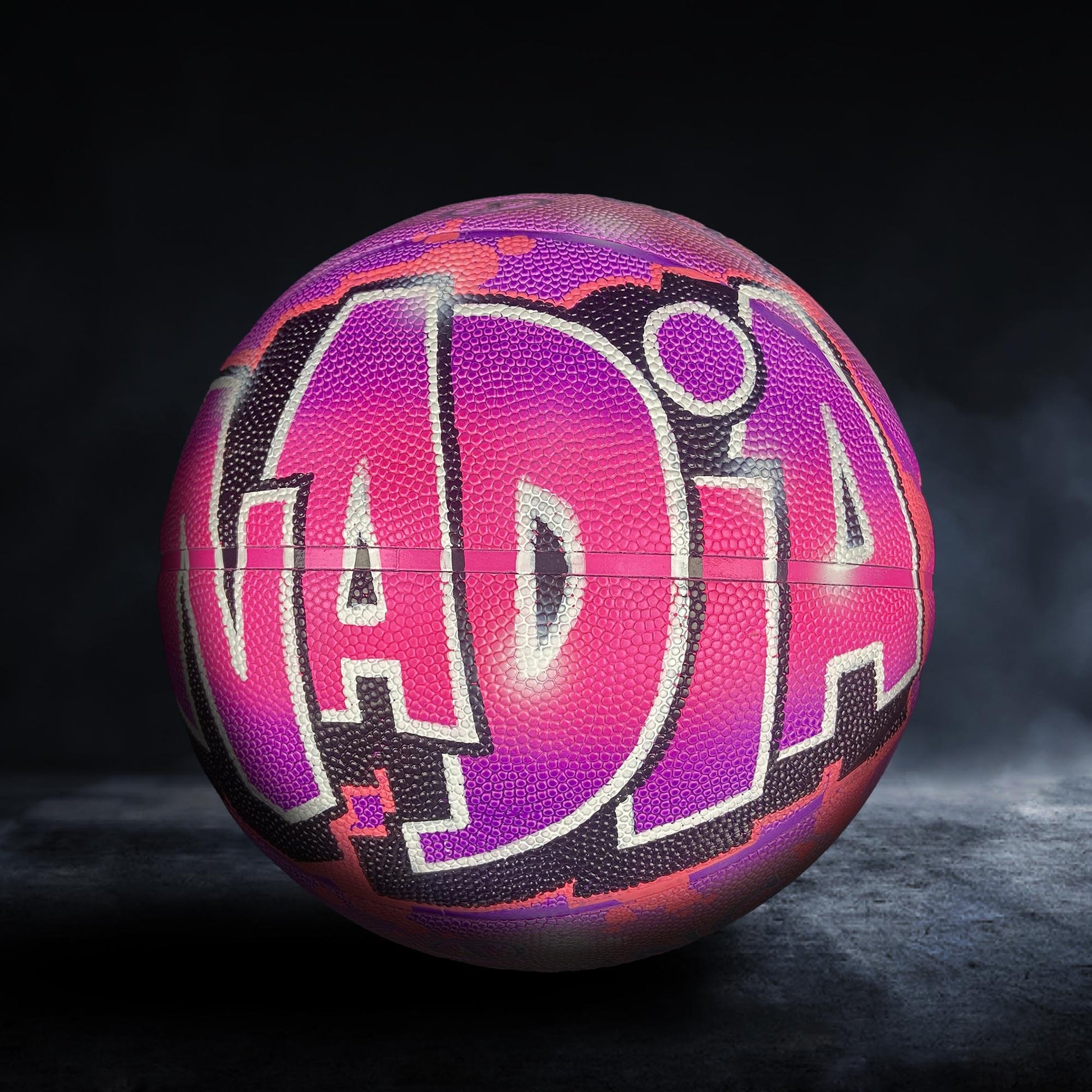 A colorful basketball with the word "ADIA" painted on it, set against a dark background.