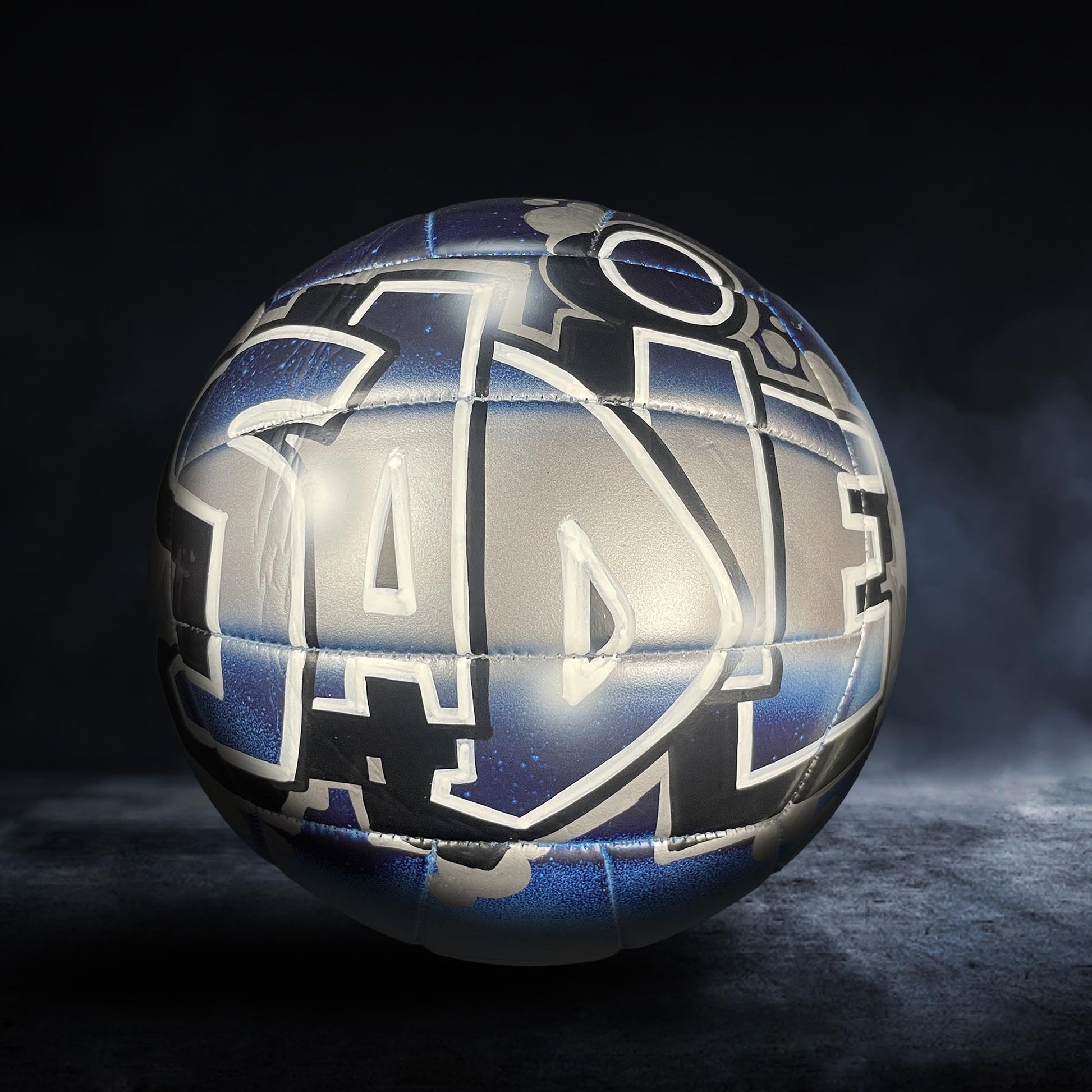 A soccer ball with a unique, graffiti-style design on it, featuring various shapes and patterns in shades of blue and gray.