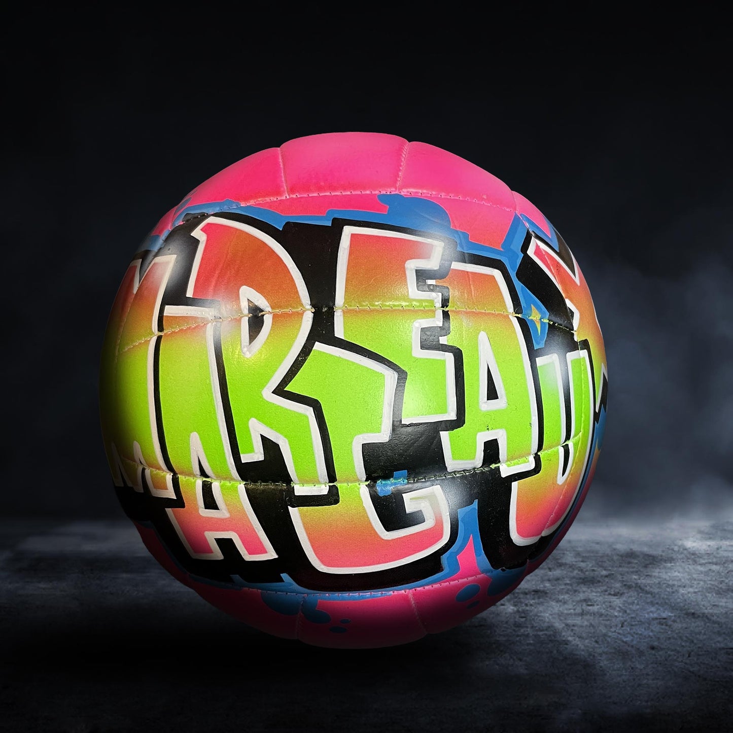 A colorful sports ball with the word "REAL" painted on it, set against a dark background.