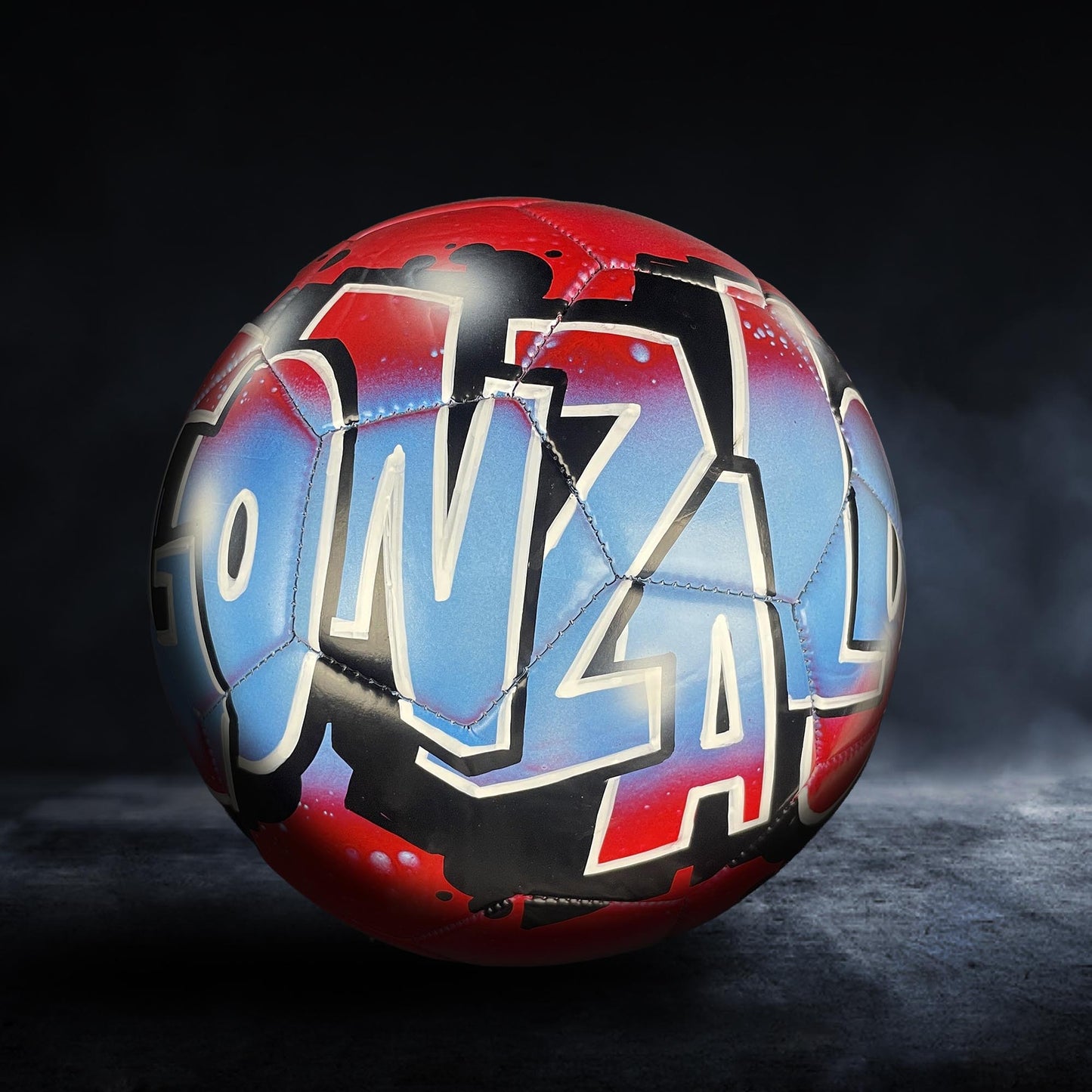 A soccer ball with graffiti-style lettering on it, set against a dark background.