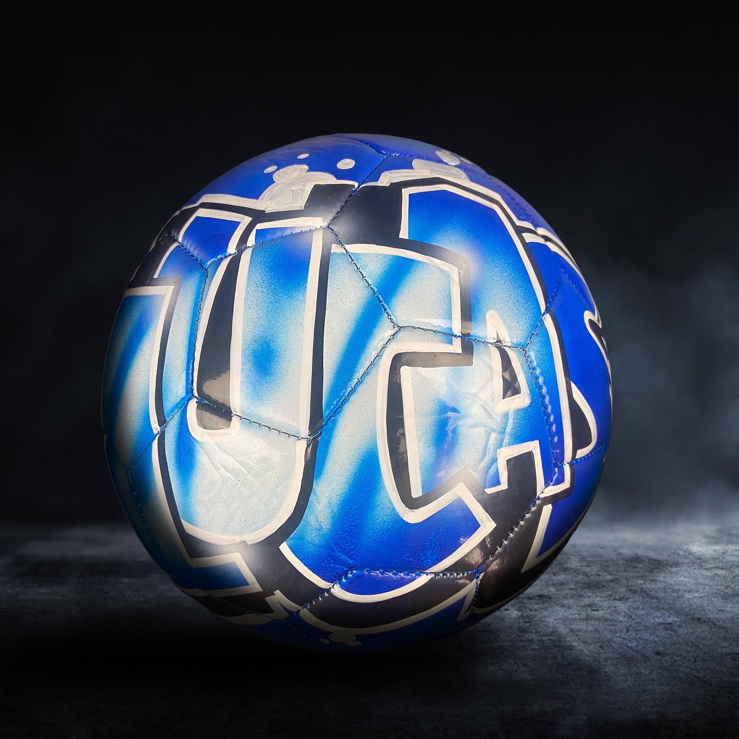 A blue and white soccer ball with a stylized design on it, placed on a dark surface.