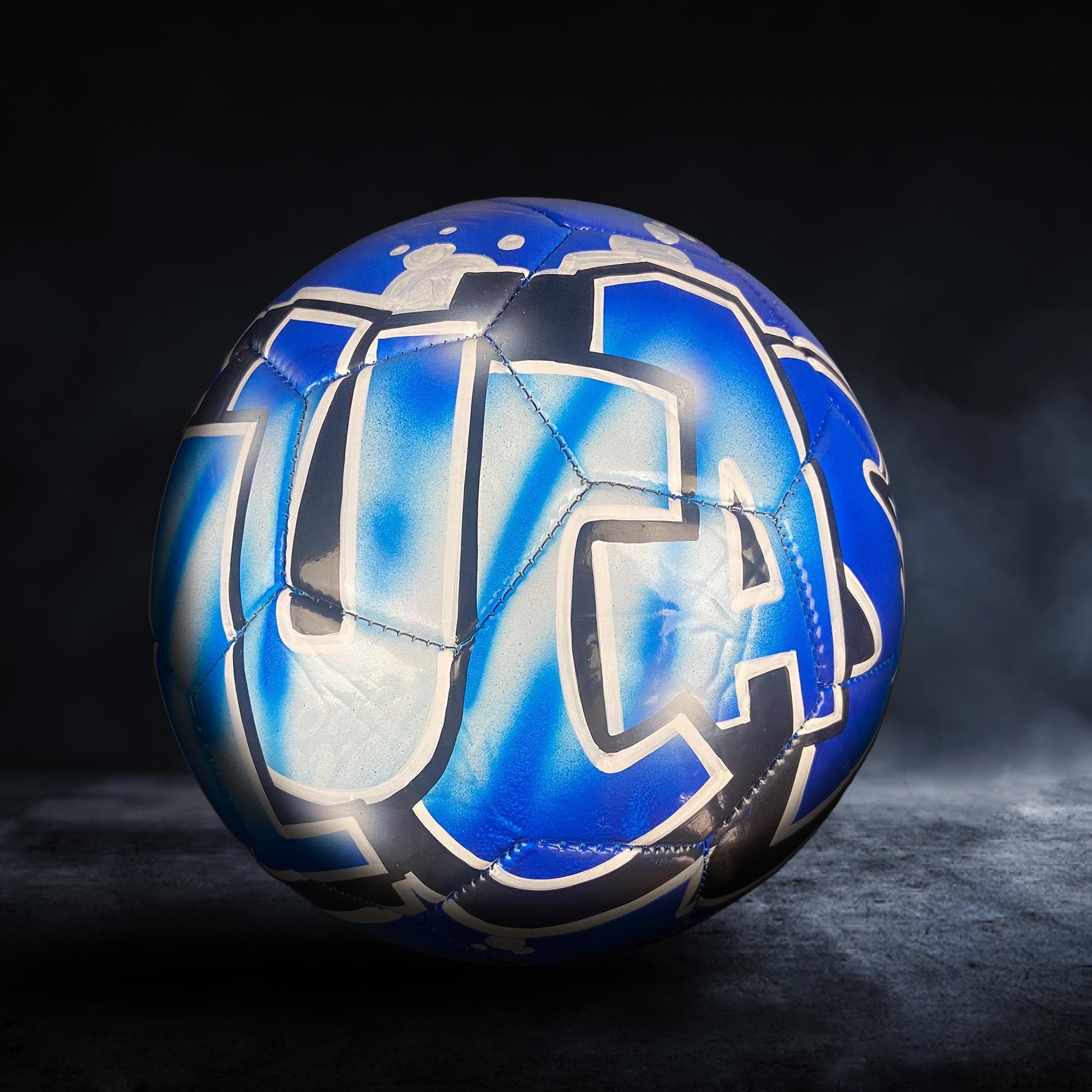 A blue and white soccer ball with a stylized design on it, placed on a dark surface.
