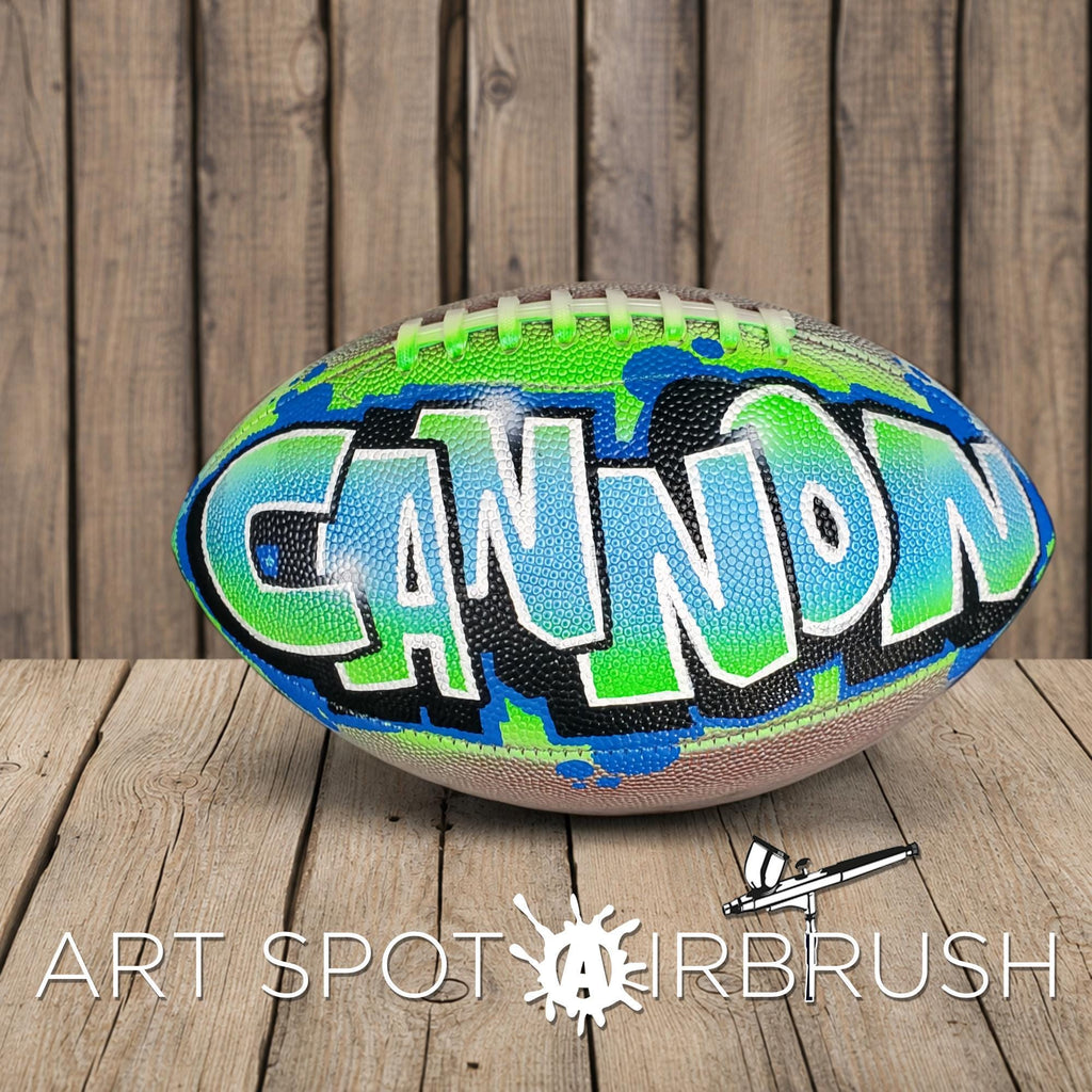 A colorful football with the word "CANNON" painted on it, sitting on a wooden surface.