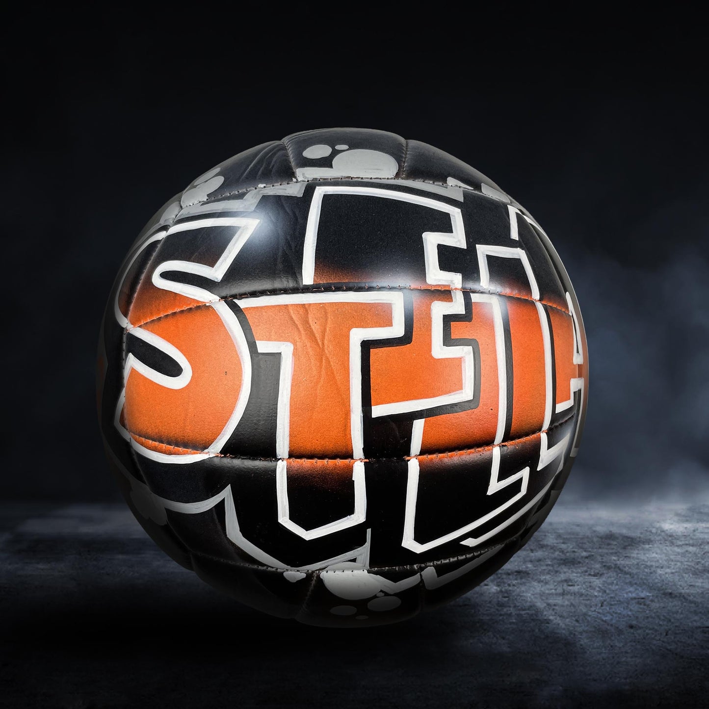 A soccer ball with the word "STEEL" painted on it, set against a dark background with smoke or fog.