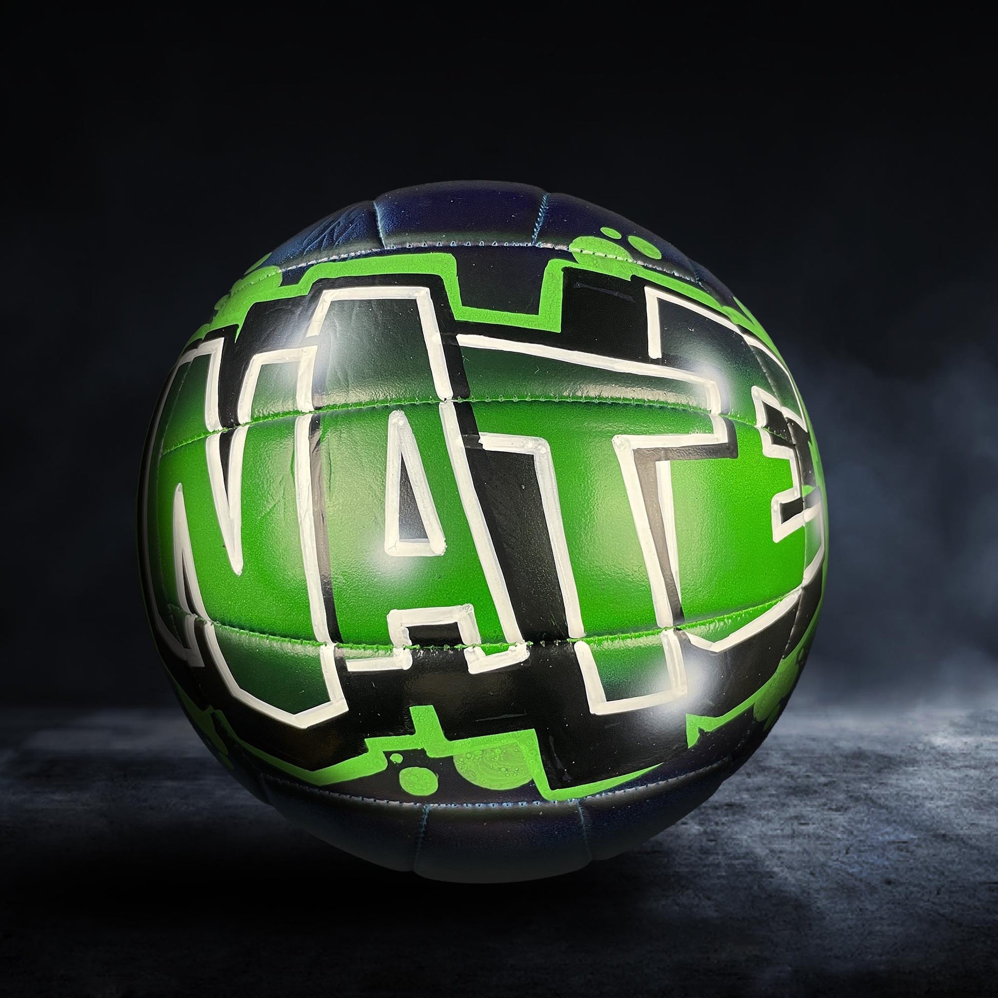 A green and black soccer ball with the word "NATE" painted on it.