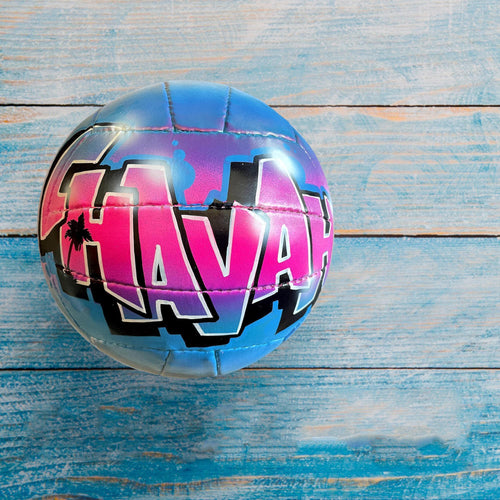 A custom volleyball with the word "HAV" written on it, placed on a blue wooden surface.