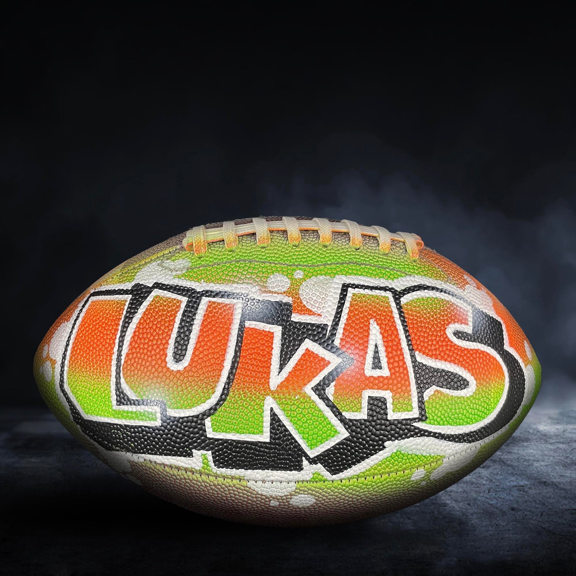 A football with the name "LUKAS" painted on it, featuring a colorful and stylized design.