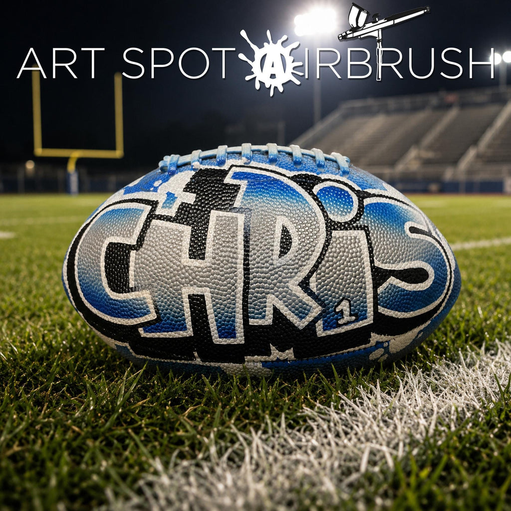A personalized custom football with the name "CHRIS" painted on it, placed on a grassy field with a football field and stadium in the background.