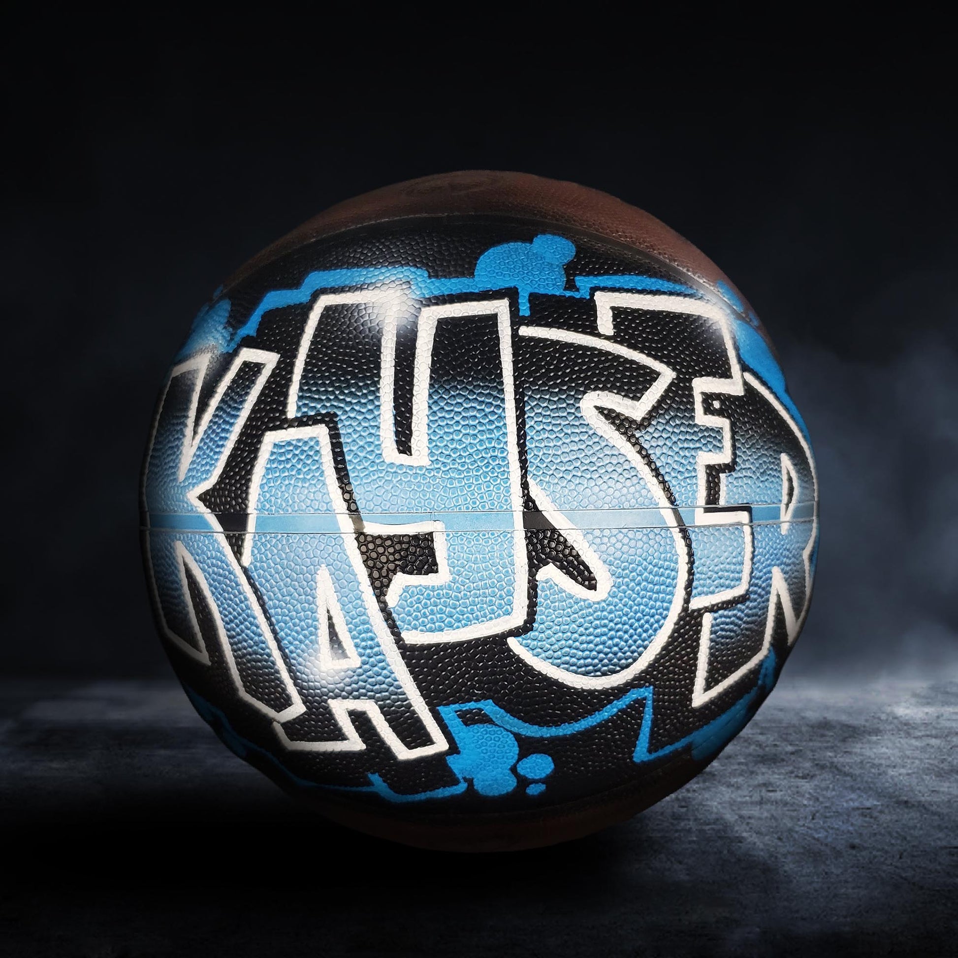 A basketball with the word "KASER" painted on it in blue and black graffiti-style lettering.
