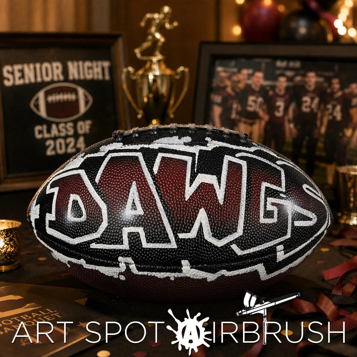 a custom football personalized with the word "DAGS" written on it, placed on a table with a framed picture of a football team in the background.