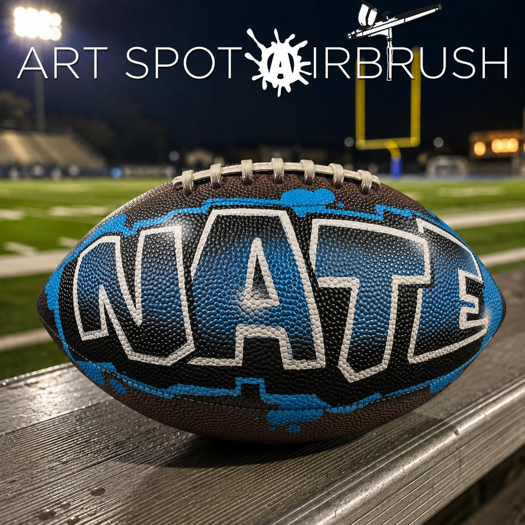 A custom football personalized with the word "NATE" painted on it, sitting on a wooden surface.