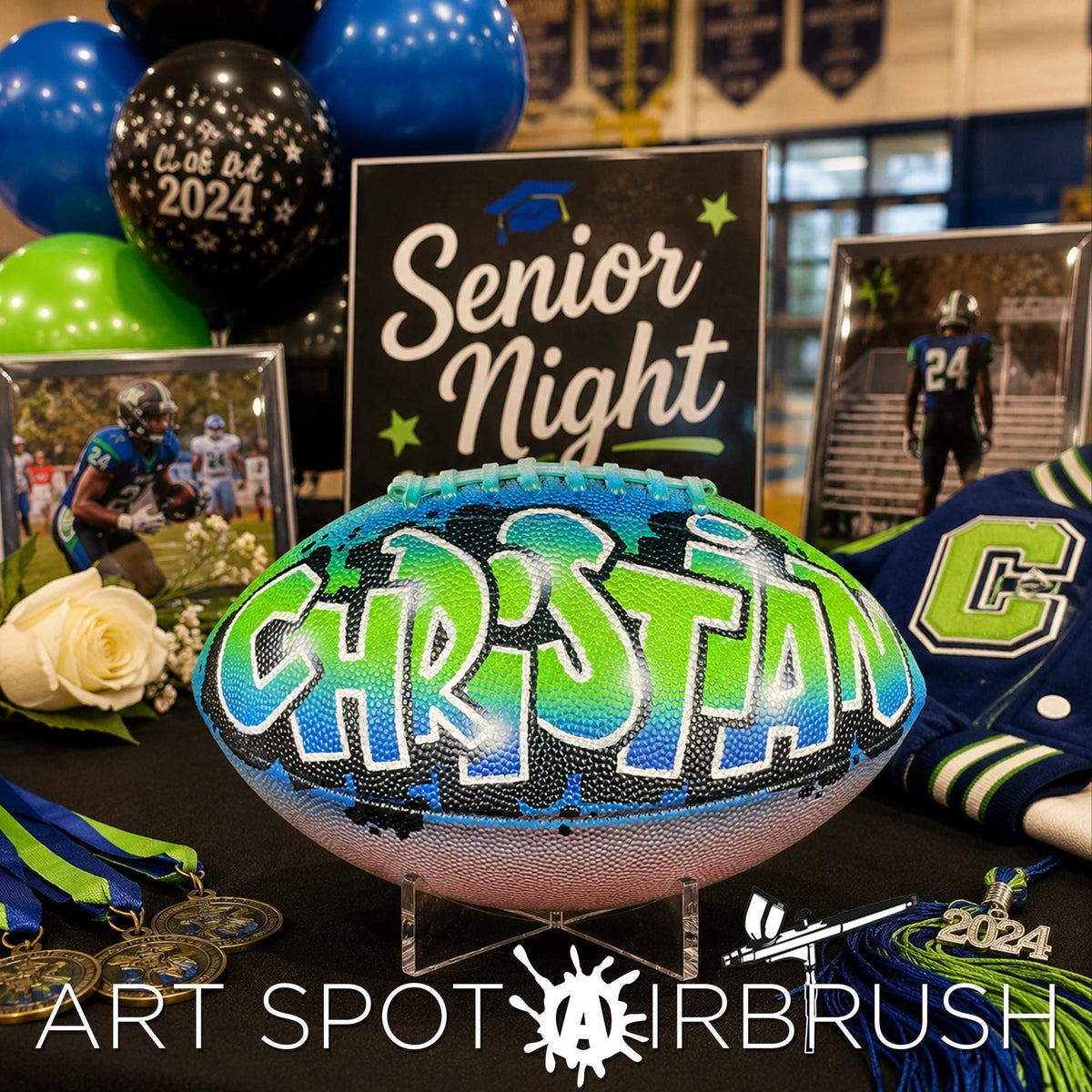 a football with the name "CHRISTIAN" painted on it, surrounded by various graduation-related items such as a framed picture, a graduation cap, and a banner that says "SENIOR NIGHT".