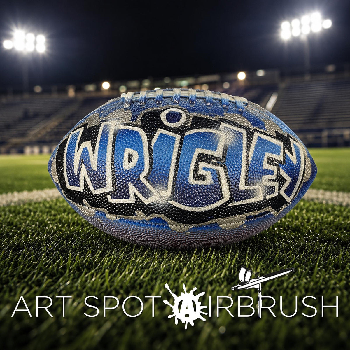 A blue and white custom football personalized with the name "WRIGLEY" written on it, placed on a grassy field with stadium lights in the background.