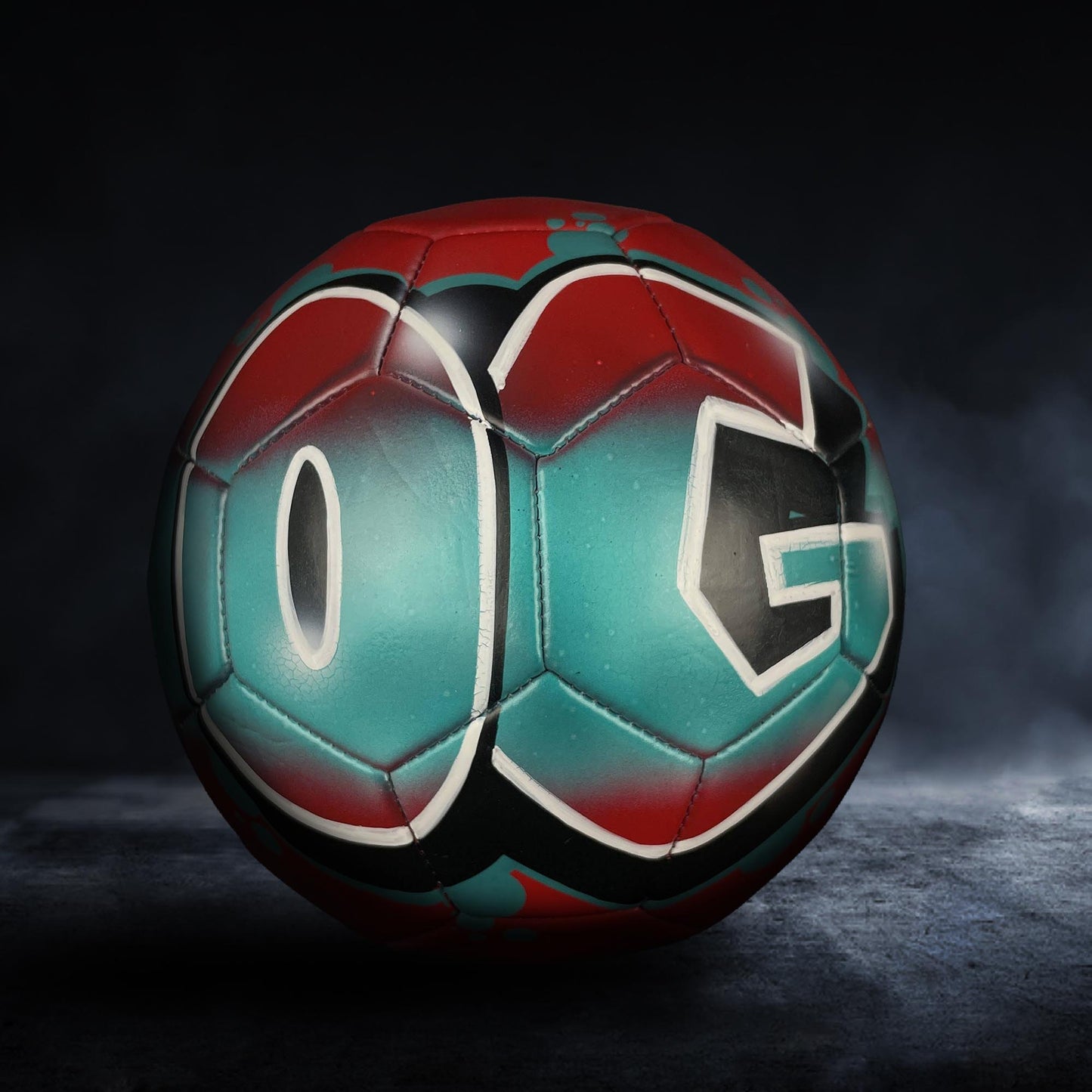 A soccer ball with the letters "OG" painted on it, set against a dark background.