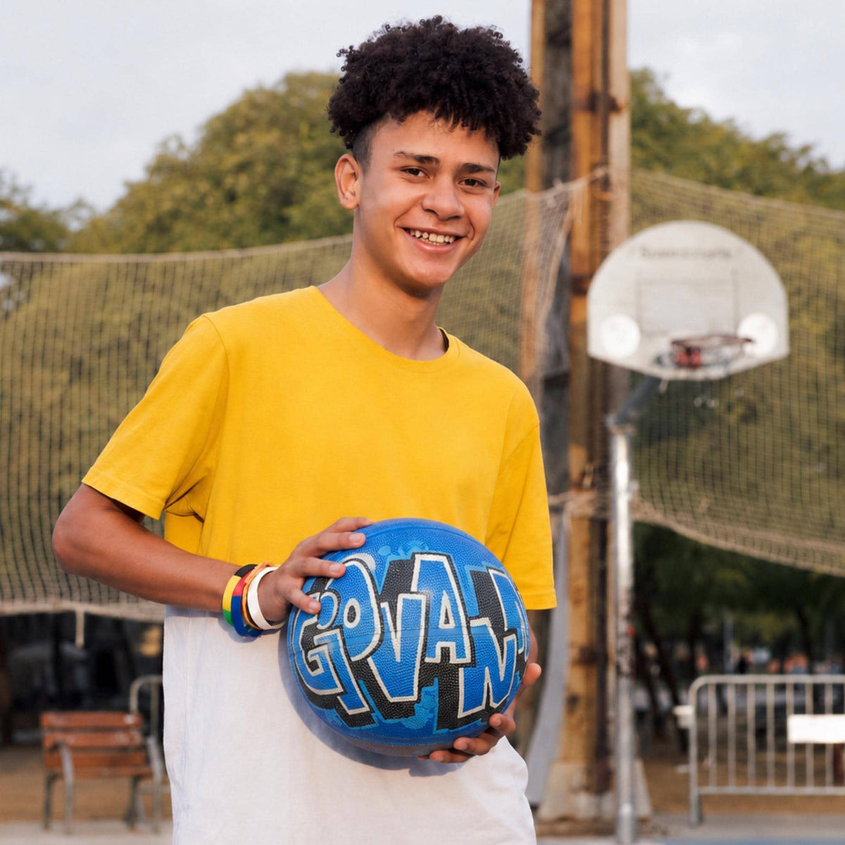 A young man in a yellow shirt is holding a blue basketball with the word "GOVAN" written on it, smiling at the camera.