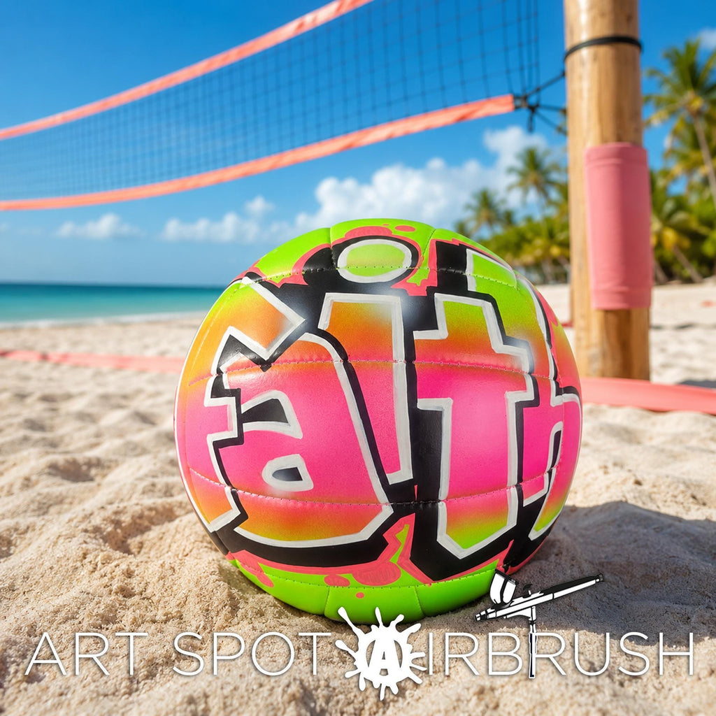 A colorful beach volleyball with the word " Faith" painted on it, resting on the sand near a volleyball net and palm trees.