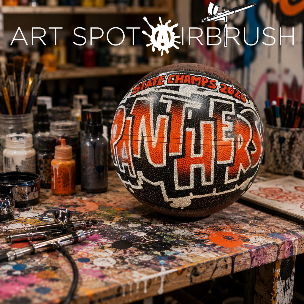 a basketball with the word "Panthers" painted on it, sitting on a table covered in paint splatters and various art supplies.