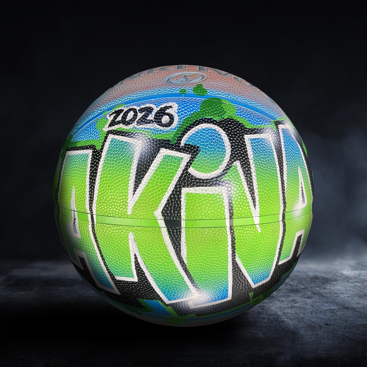 A colorful basketball with the word "AKINA" painted on it, featuring a mix of green, blue, and orange colors.